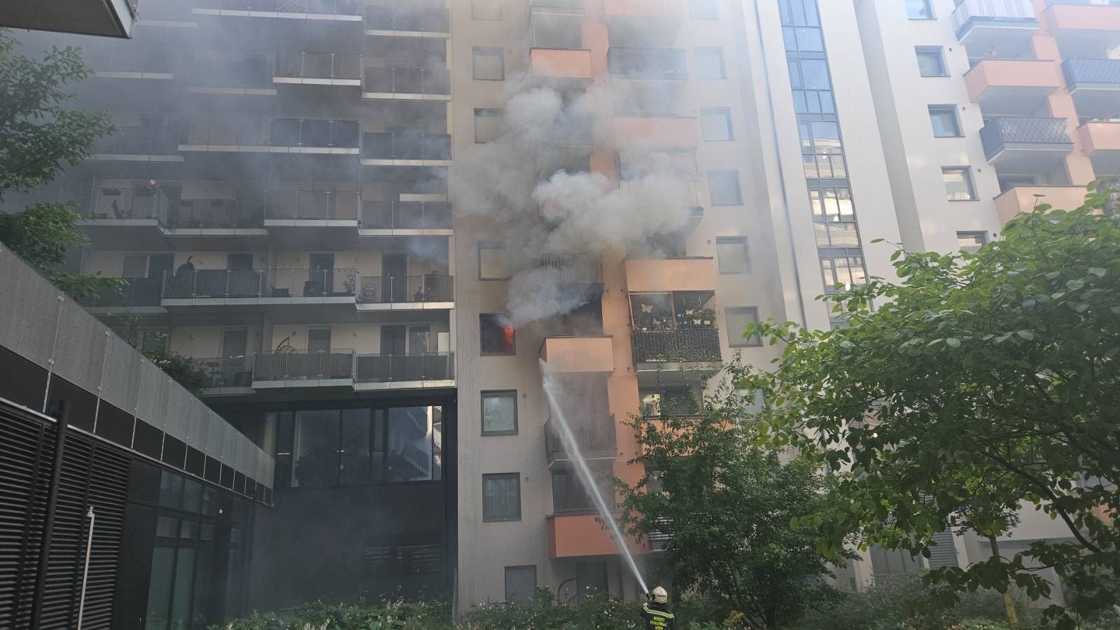 Ein Feuerwehrmann löscht einen Zimmerbrand in einem Hochhaus, dichter Rauch steigt auf.