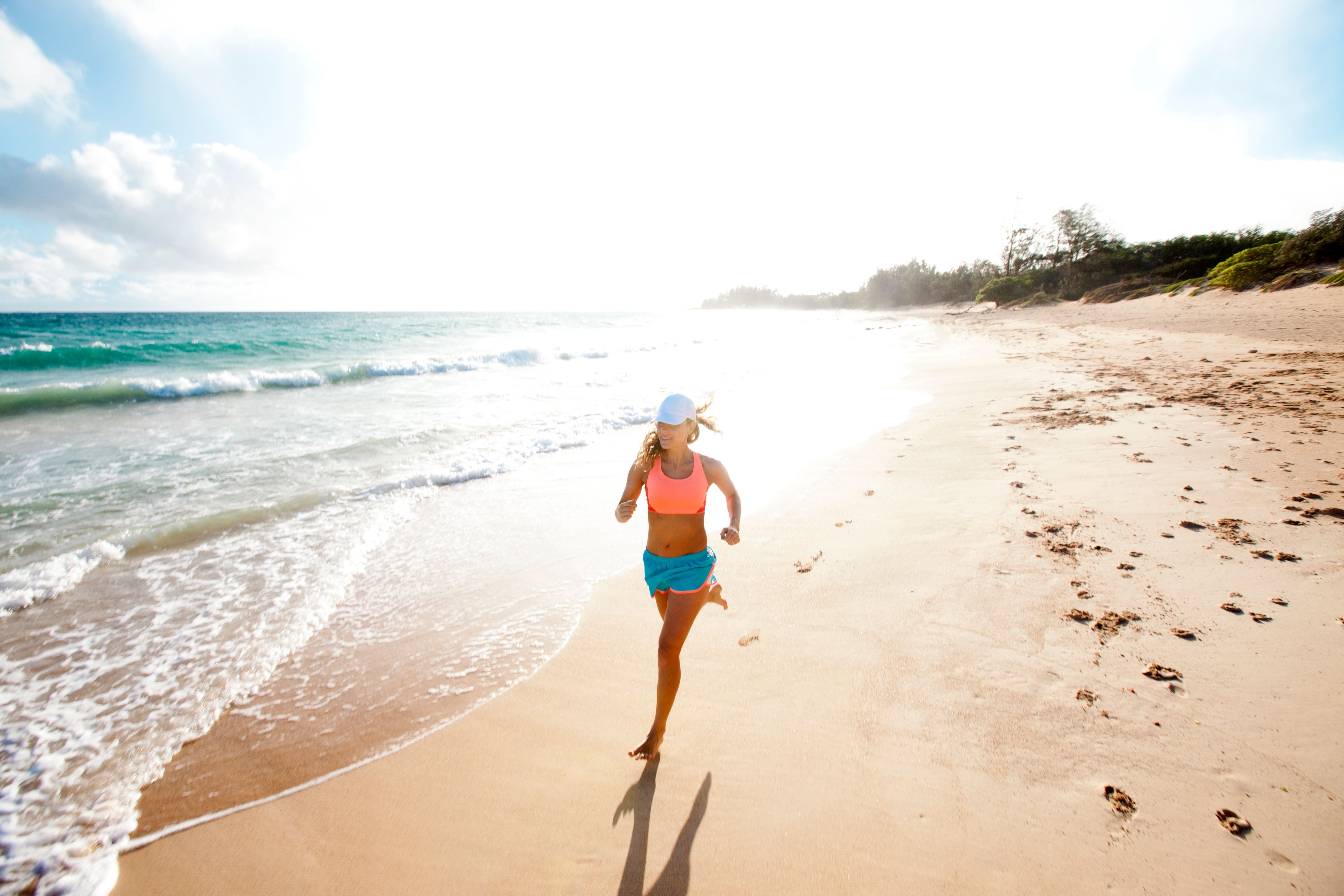 Frau joggt am sonnigen Sandstrand einer tropischen Insel entlang der Küste.