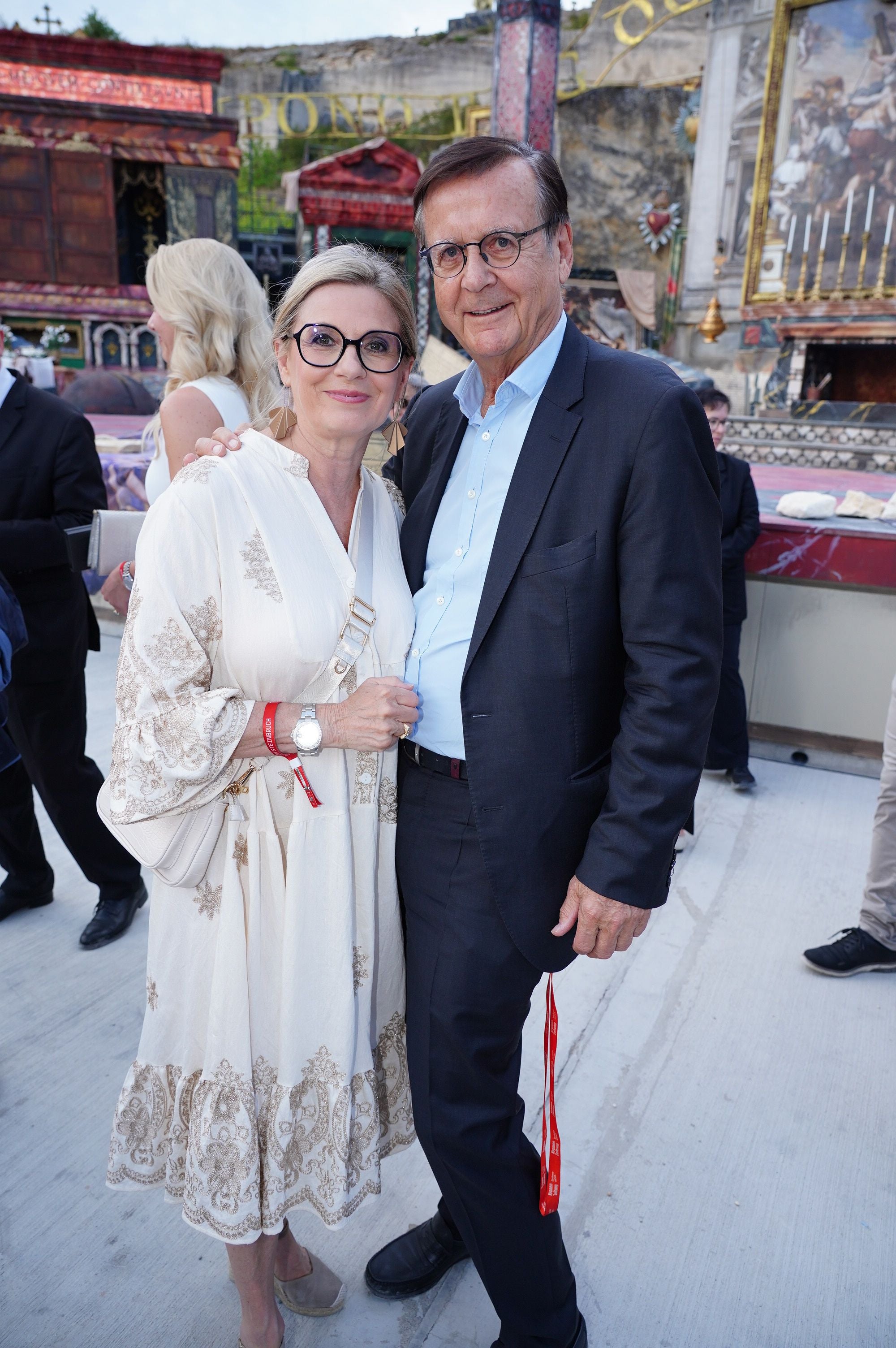 Ein elegant gekleidetes Paar posiert lächelnd bei der Tosca-Premiere im Freien.