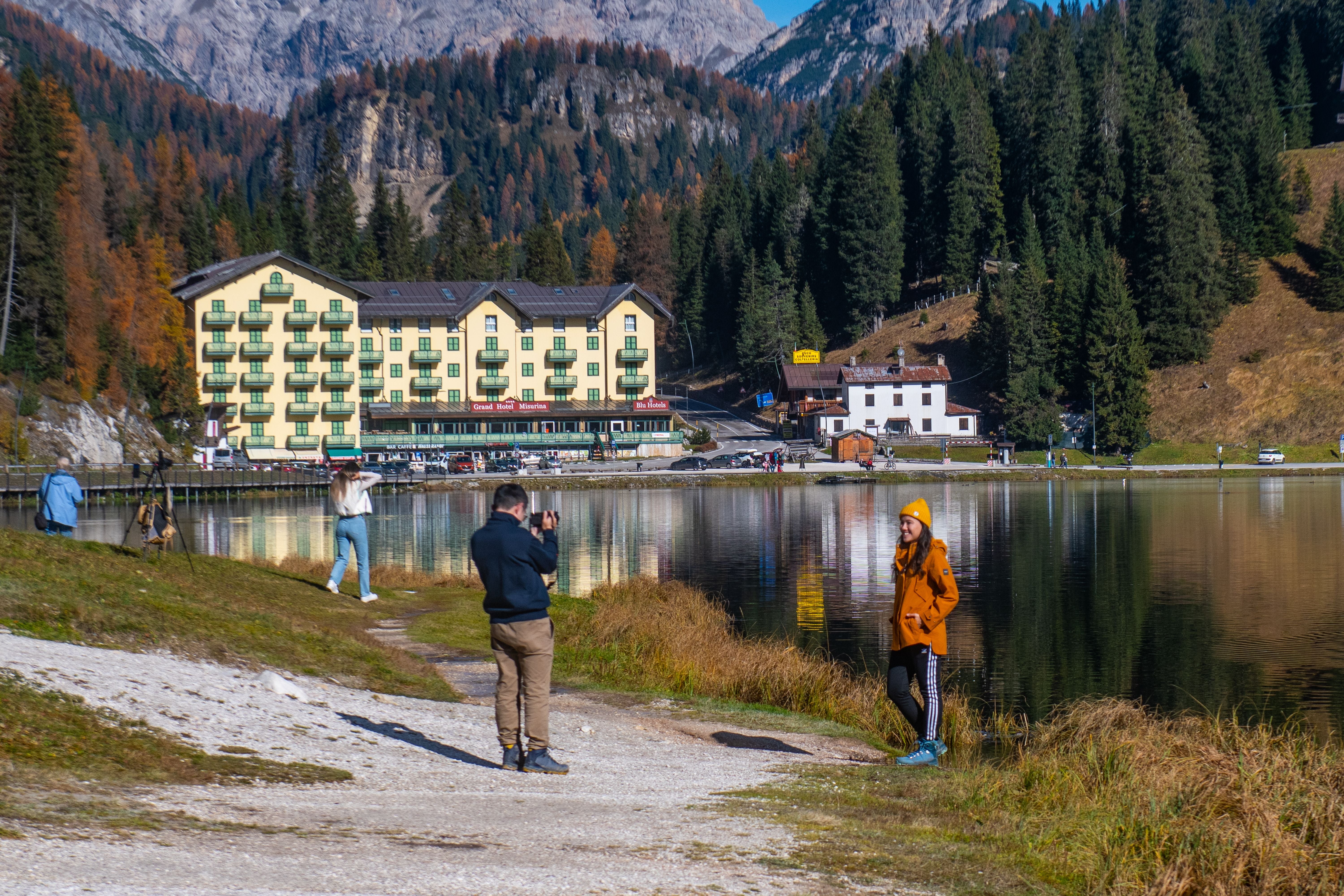 Touristen fotografieren am Ufer des Misurina-Sees mit Hotel und Bergen im Hintergrund.