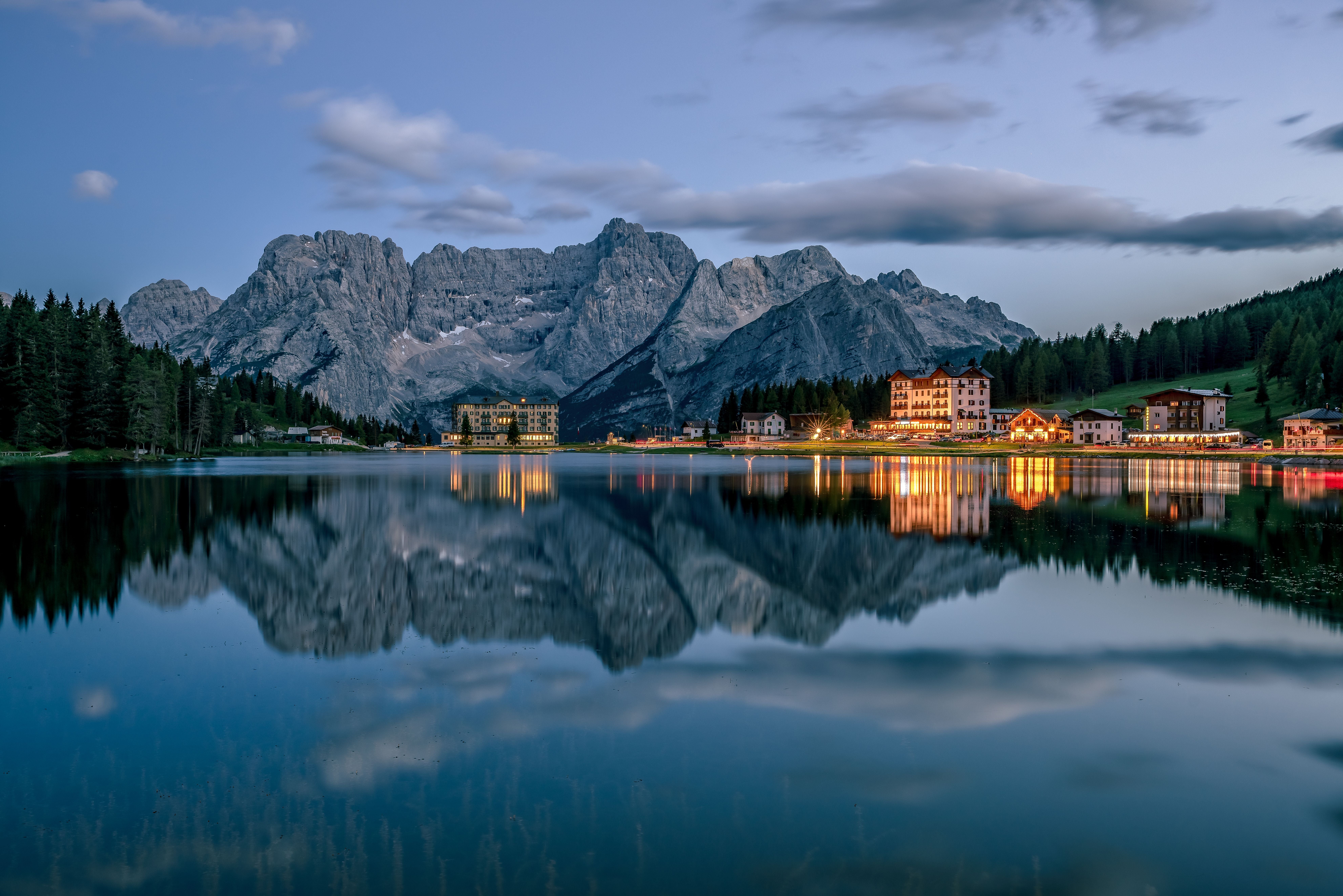 Abendstimmung am See mit Spiegelung der Dolomiten und beleuchteten Gebäuden am Ufer.
