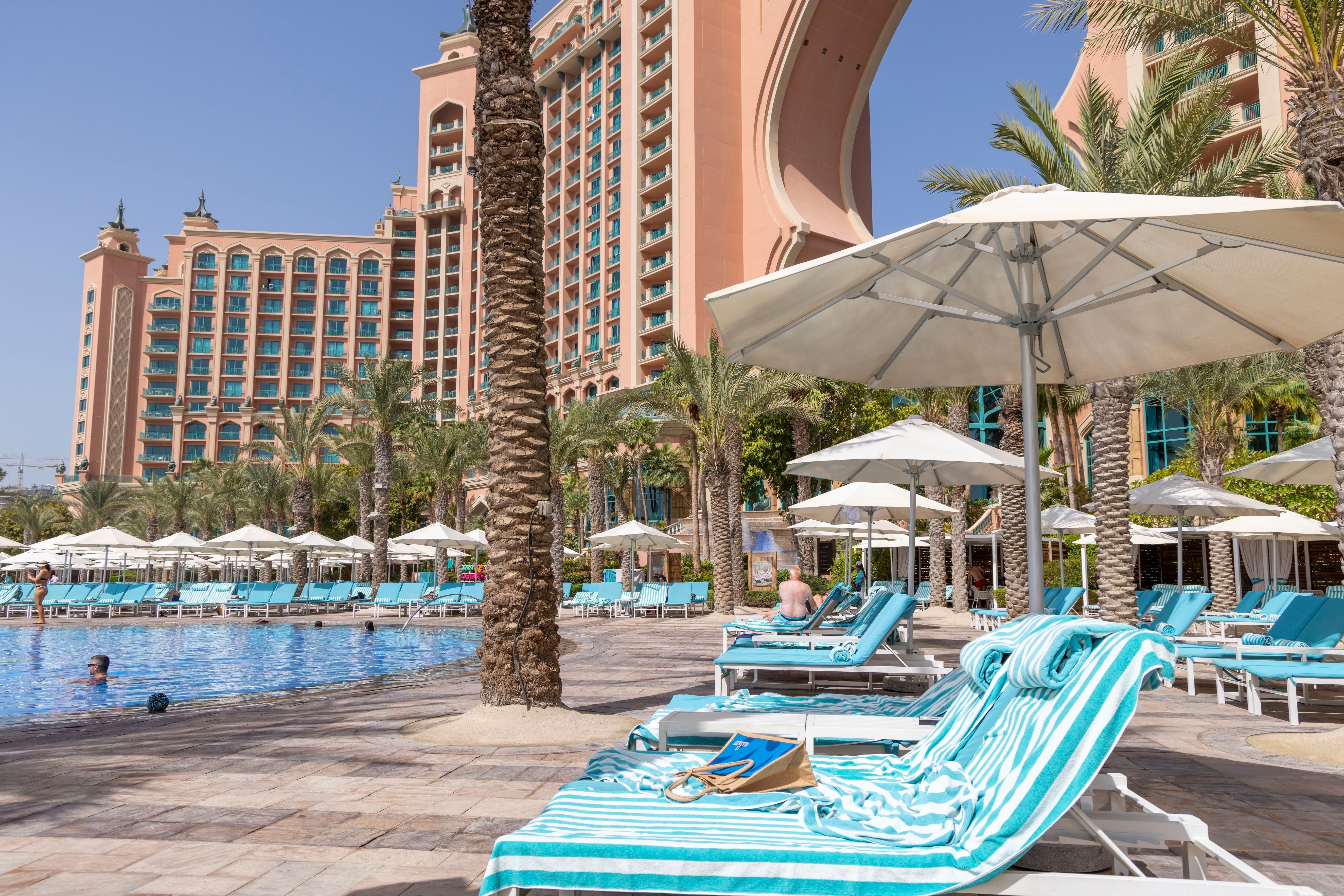 Poolbereich mit Sonnenliegen und Schirmen vor dem Atlantis The Palm Hotel in Dubai bei sonnigem Wetter.