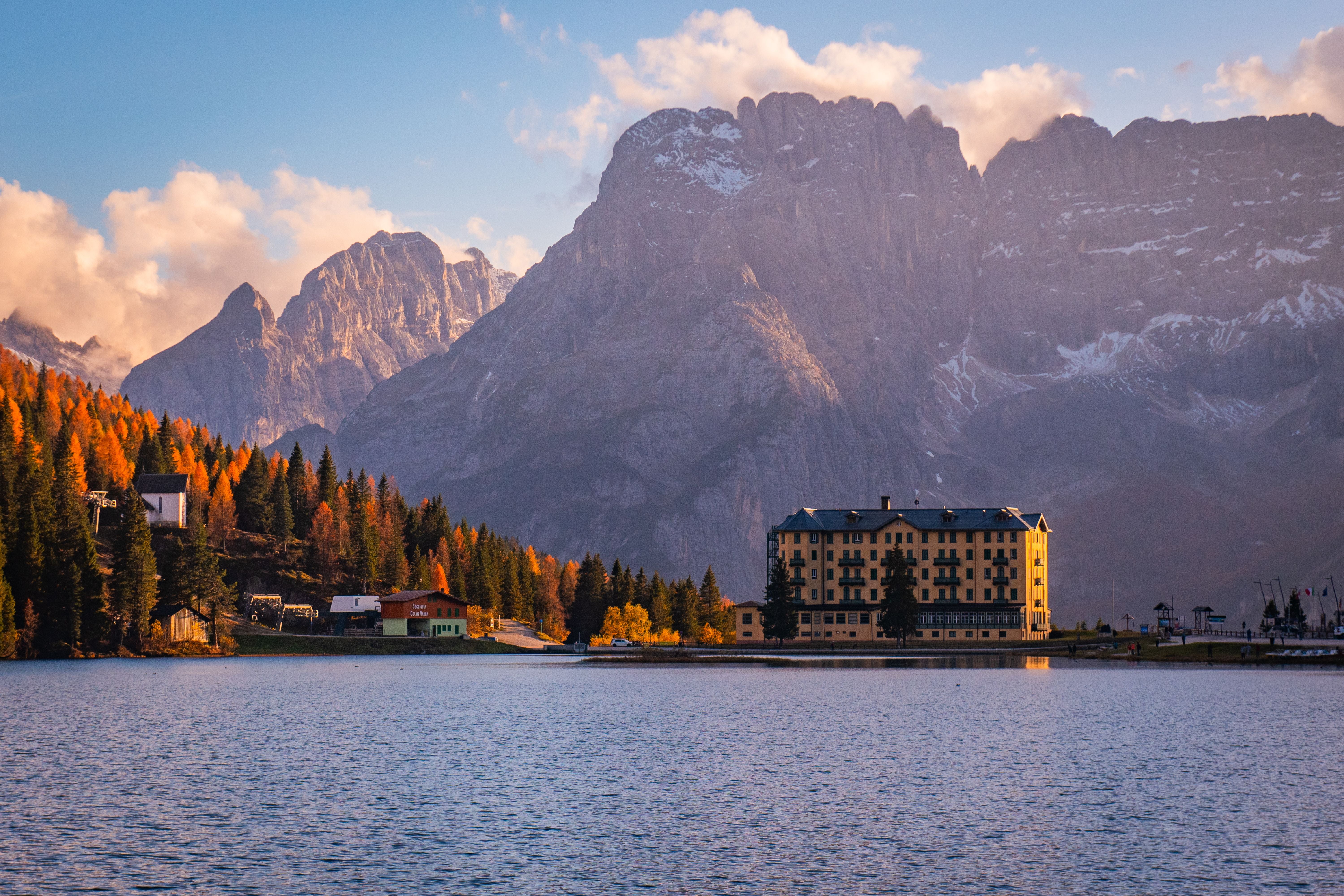 Herbstliche Bäume und ein Hotel am Ufer des Misurina-Sees, im Hintergrund die Dolomiten.