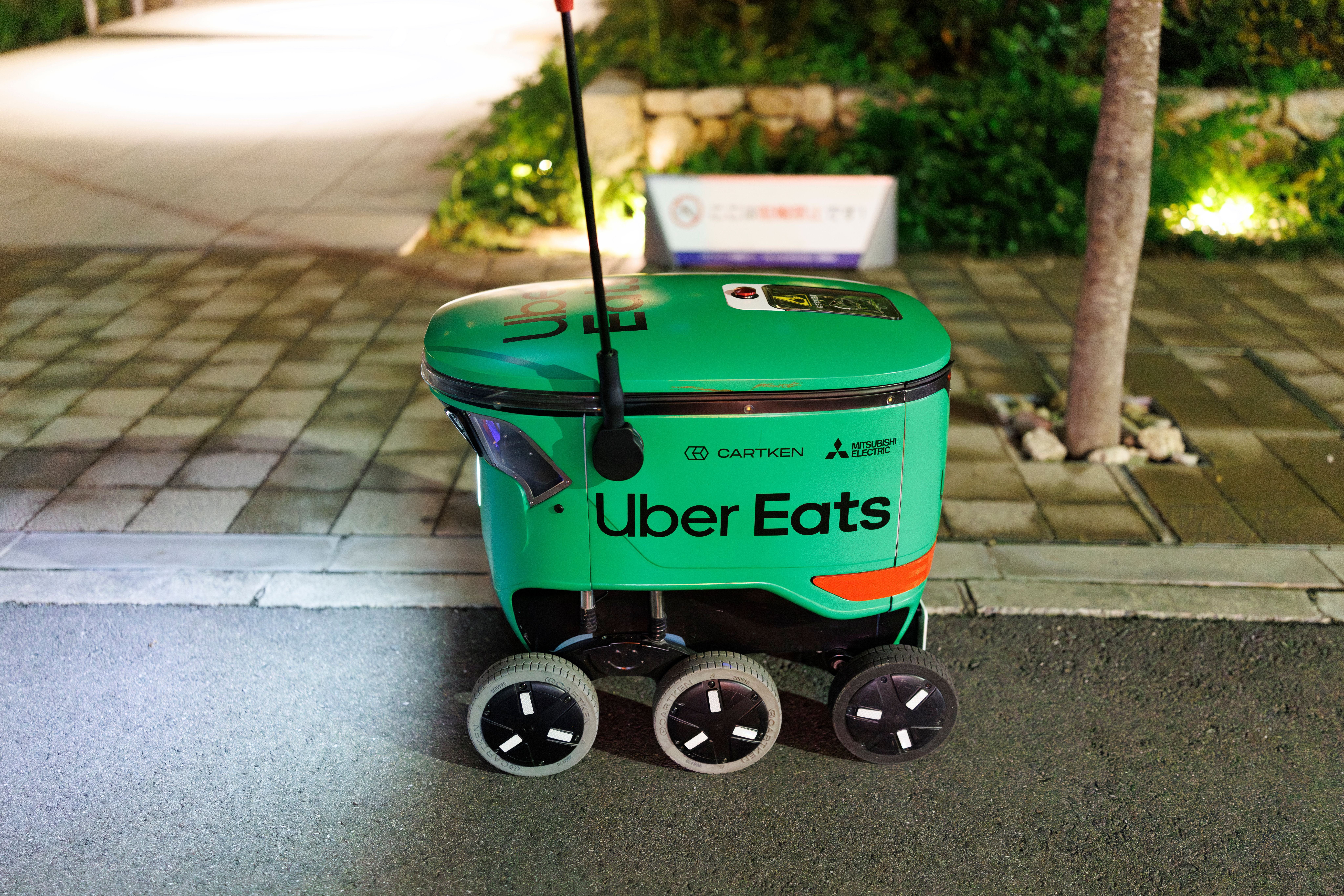 Ein selbstfahrender Uber Eats Lieferroboter steht nachts auf einem Bürgersteig in Osaka.