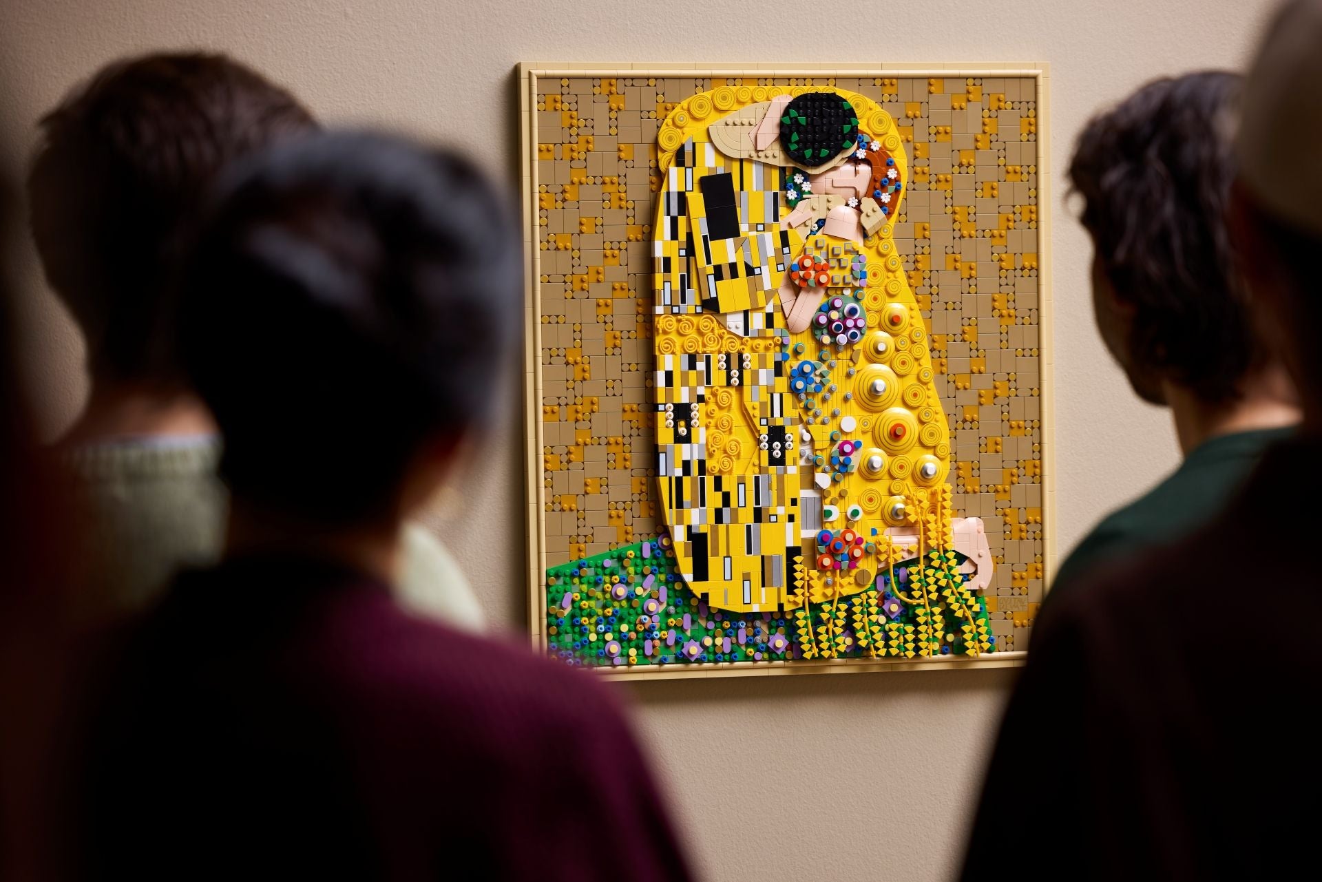 Mehrere Personen betrachten ein LEGO®-Mosaik von Klimts „Der Kuss“ an einer Wand.