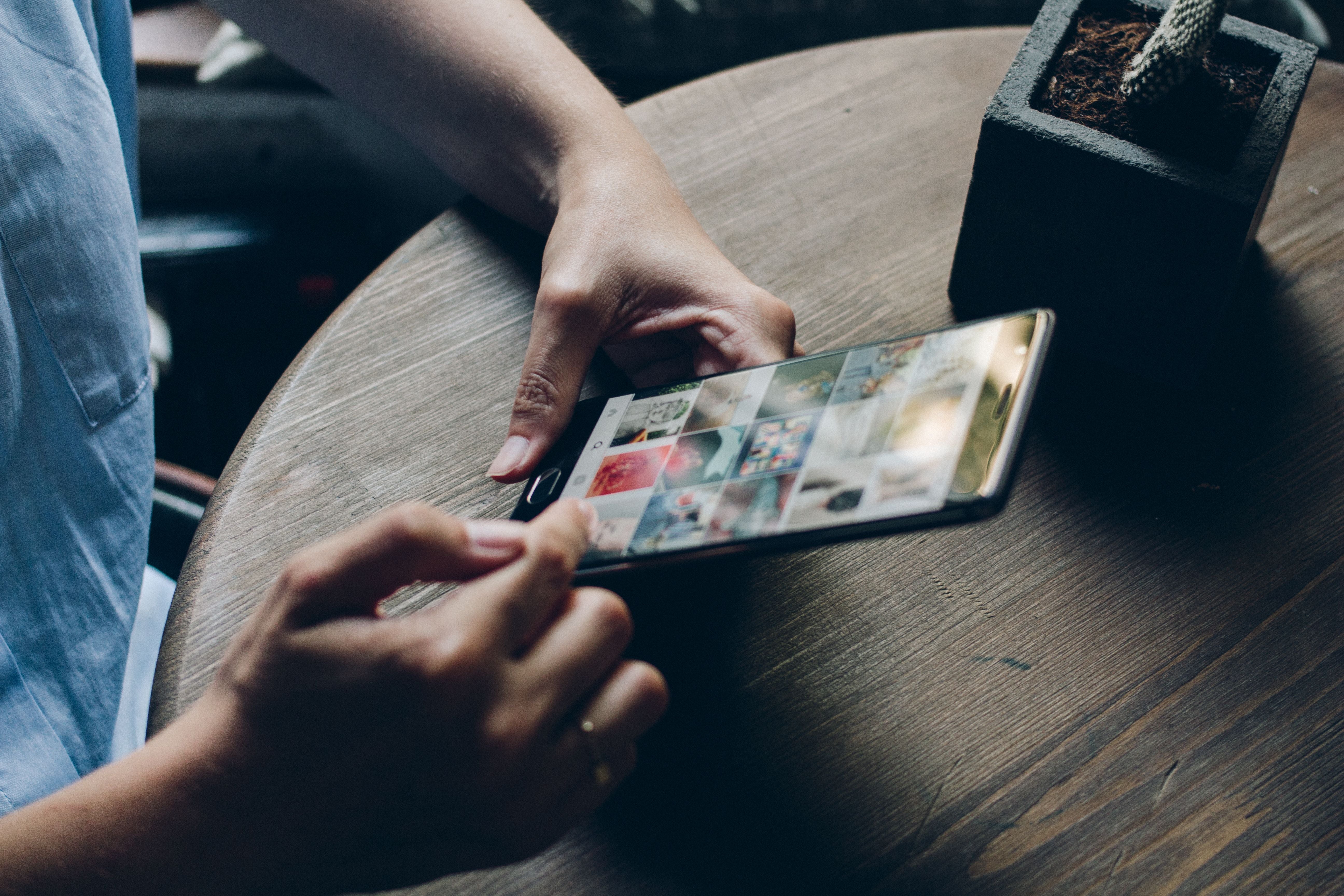 Eine Person benutzt ein Smartphone und betrachtet eine Instagram-Fotogalerie am Holztisch.