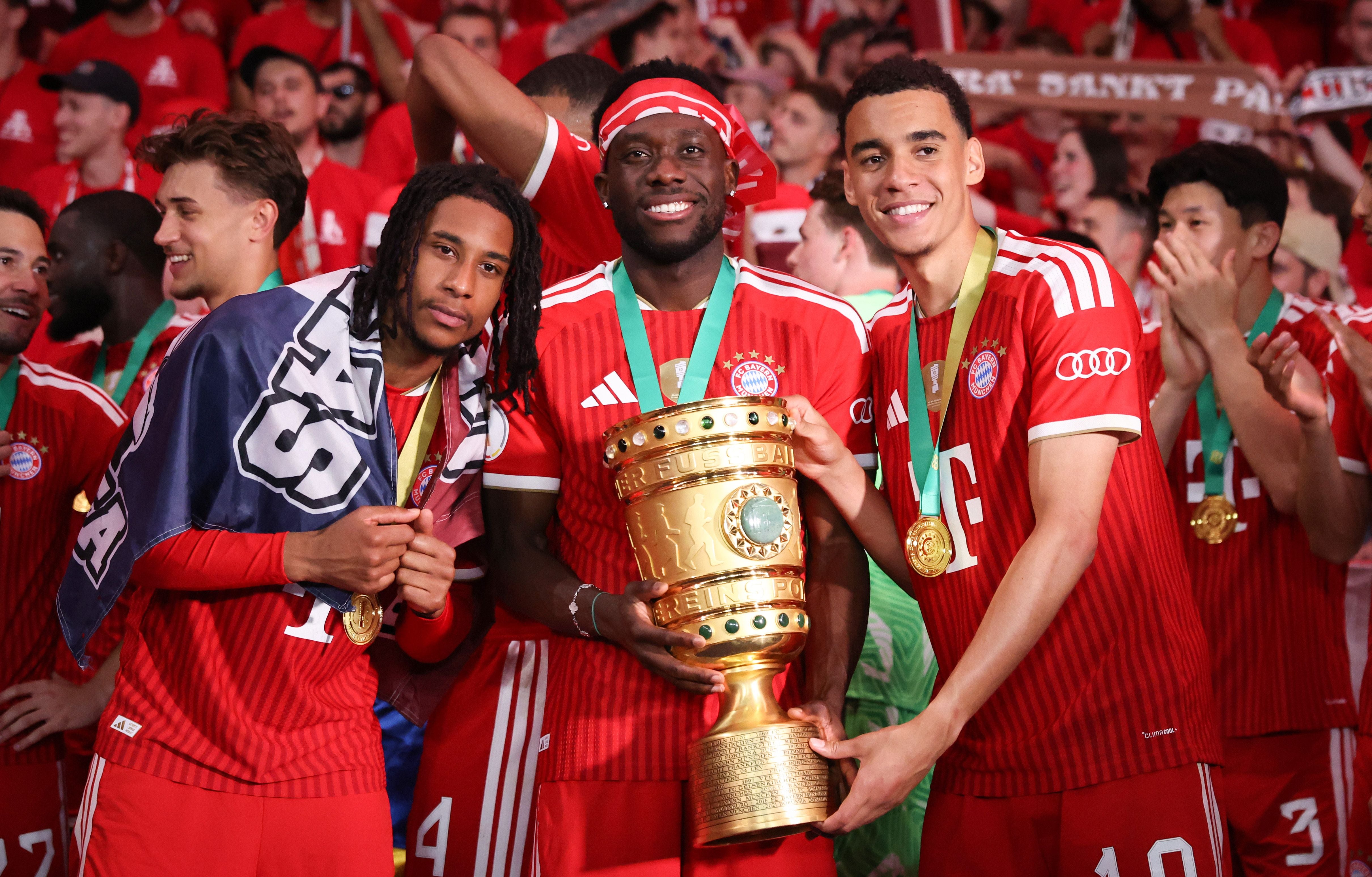 Drei Bayern-Spieler feiern mit Pokal und Goldmedaillen nach dem DFB-Pokalfinale im Stadion.