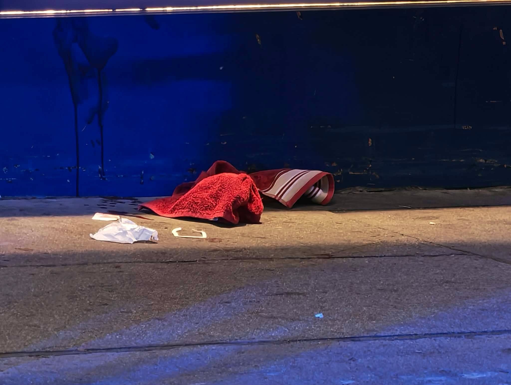 Eine rote Decke und Papier liegen auf dem Gehweg vor einer blauen Wand bei Nachtbeleuchtung.