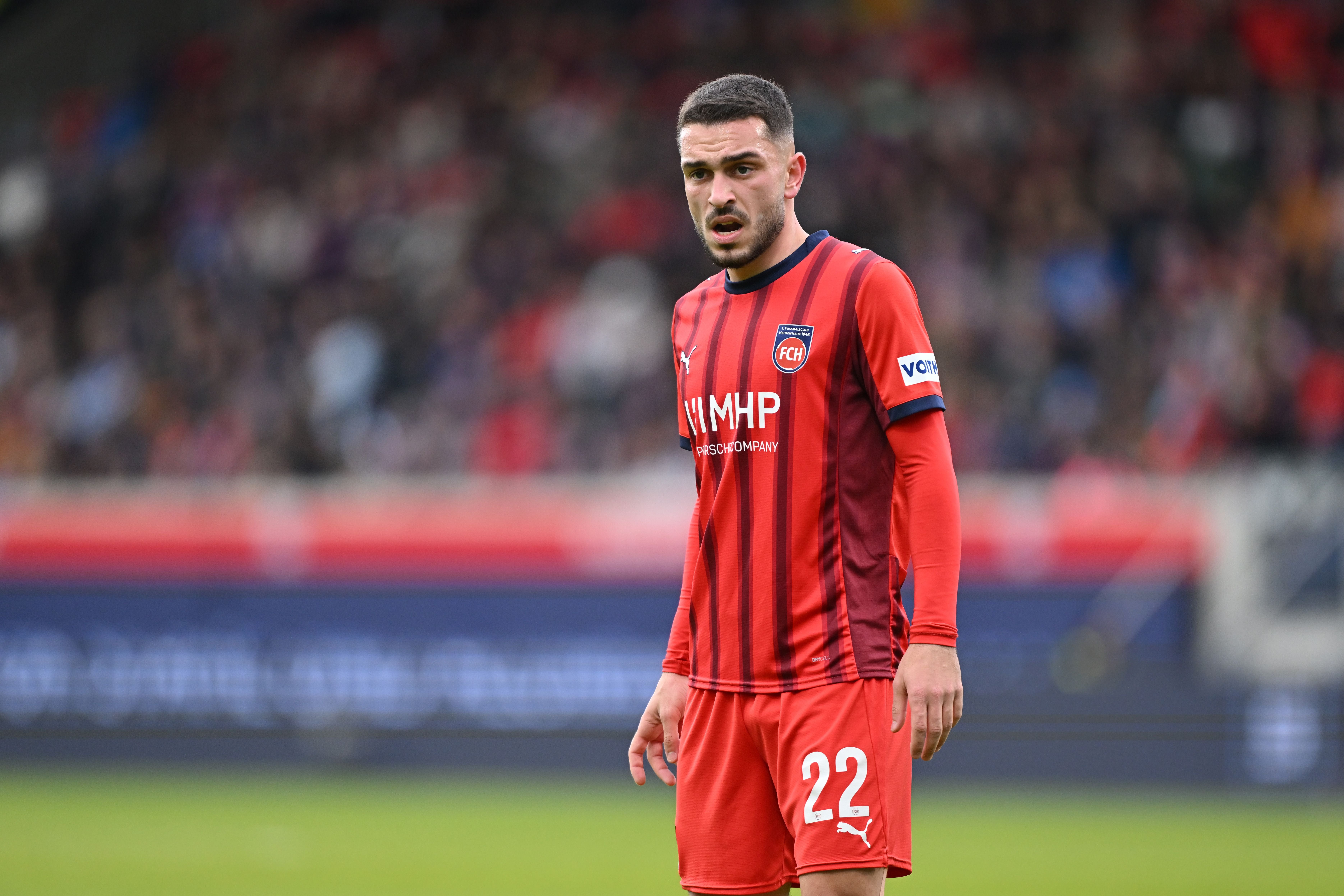 Fußballspieler im roten Trikot von Heidenheim steht auf dem Spielfeld.