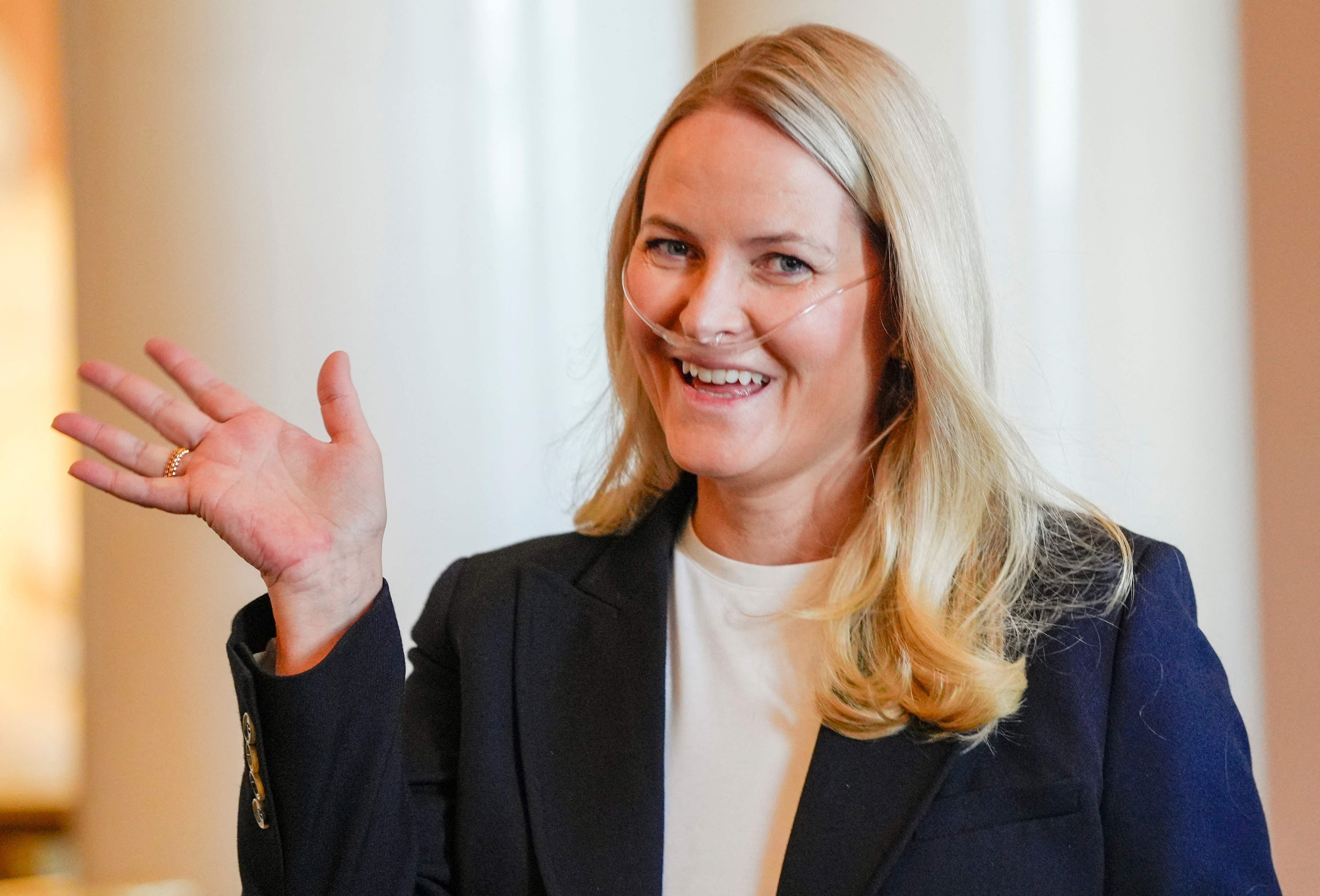 Eine lächelnde Frau mit Nasenkanüle winkt in die Kamera.