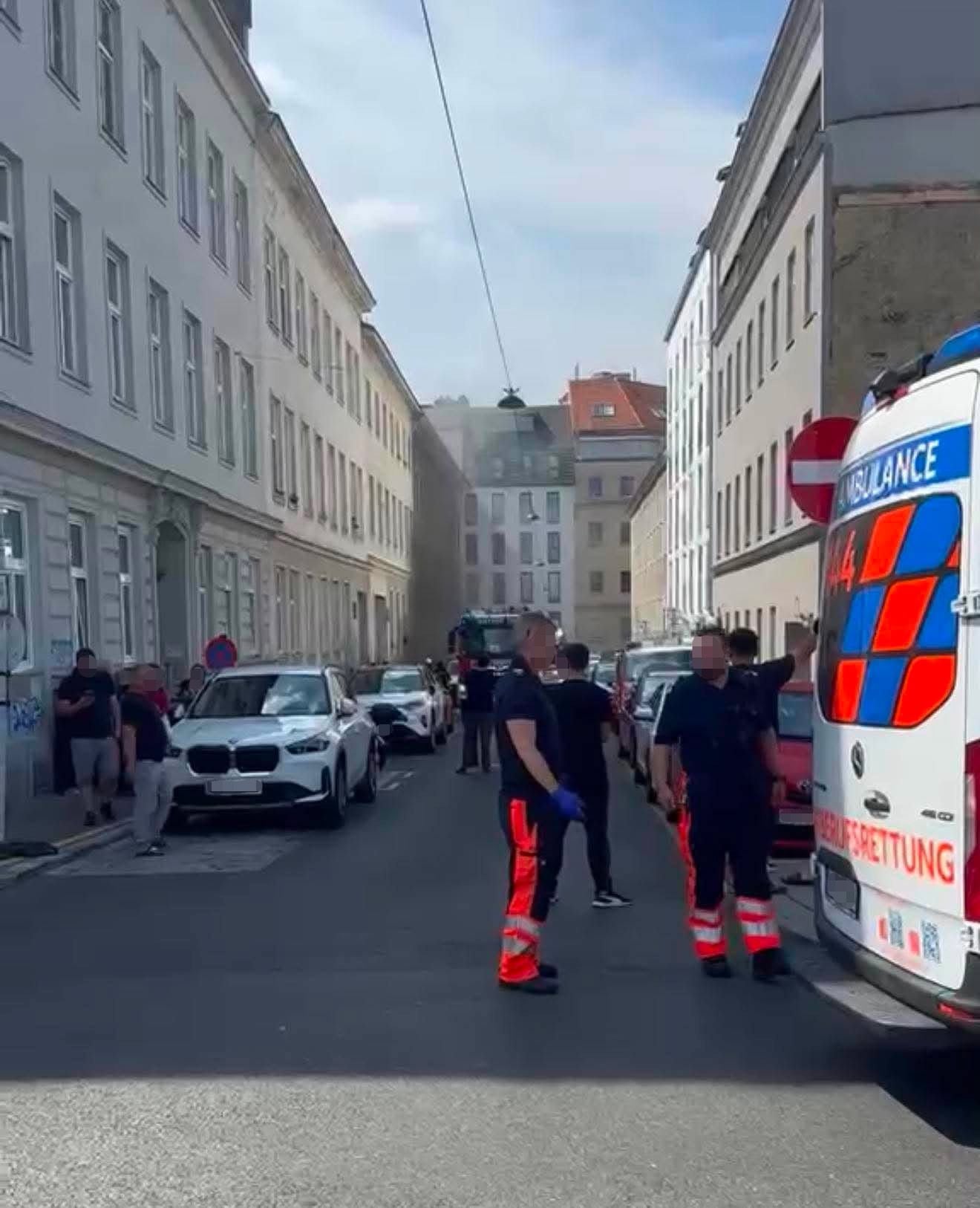 Rettungskräfte und Einsatzfahrzeuge stehen in einer Wohnstraße vor einem Gebäude mit Rauchentwicklung.