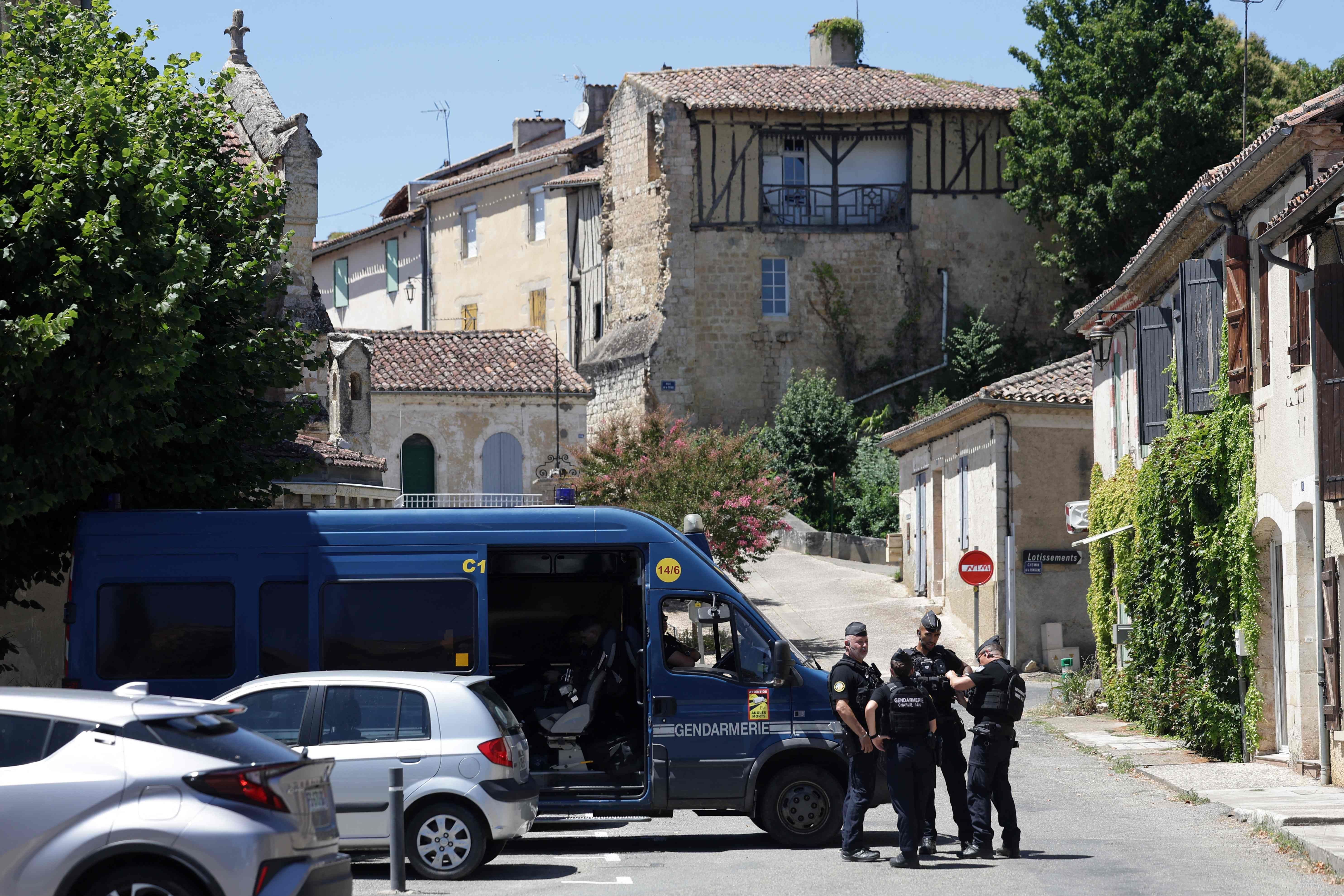Französische Polizisten sperren eine Straße in einem alten Dorf mit Einsatzfahrzeug und Häusern.