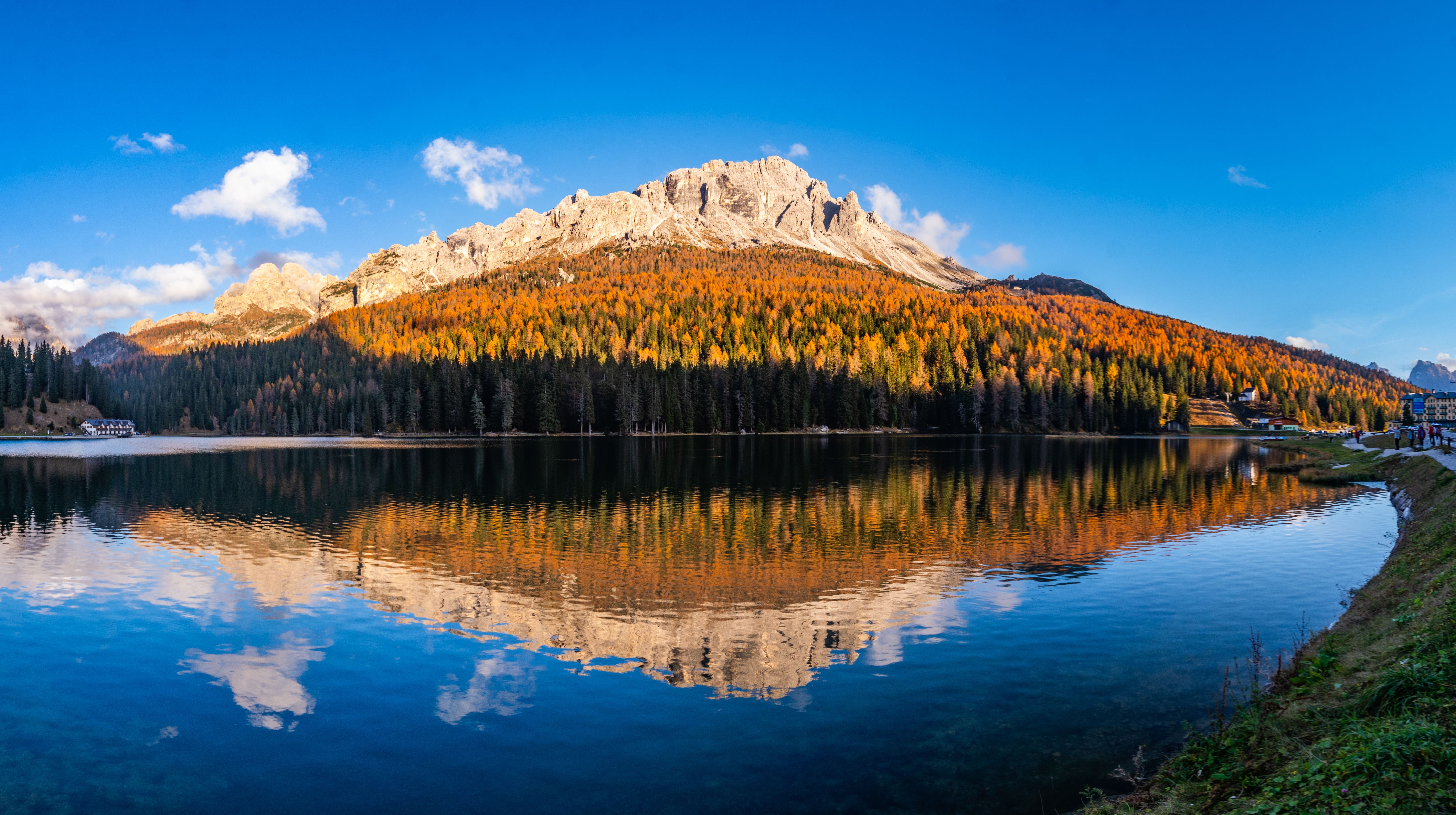 Berglandschaft mit herbstlich gefärbten Bäumen spiegelt sich in einem ruhigen See unter blauem Himmel.