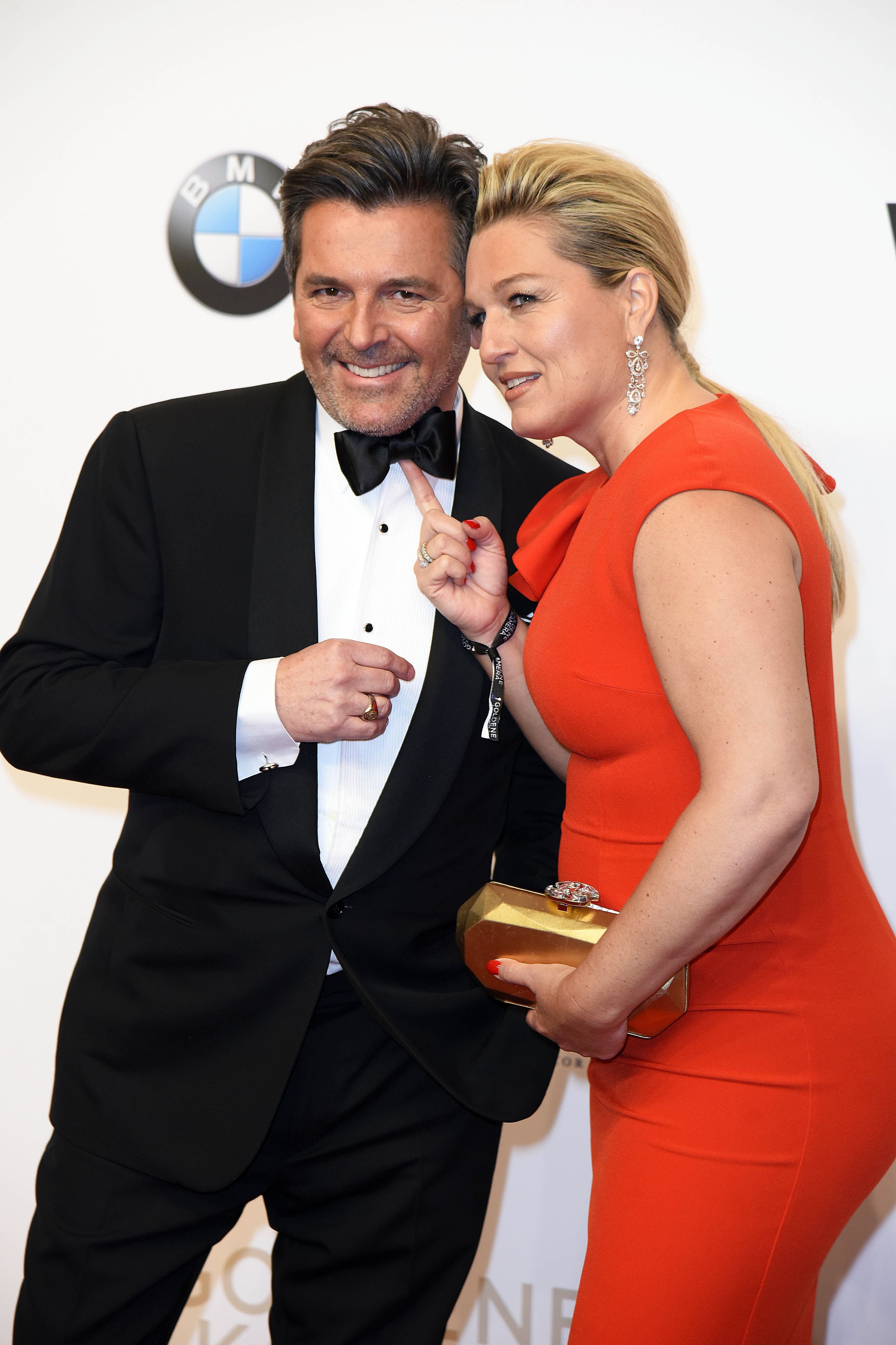 Ein Mann im Smoking und eine Frau im roten Kleid posieren gemeinsam auf dem roten Teppich.