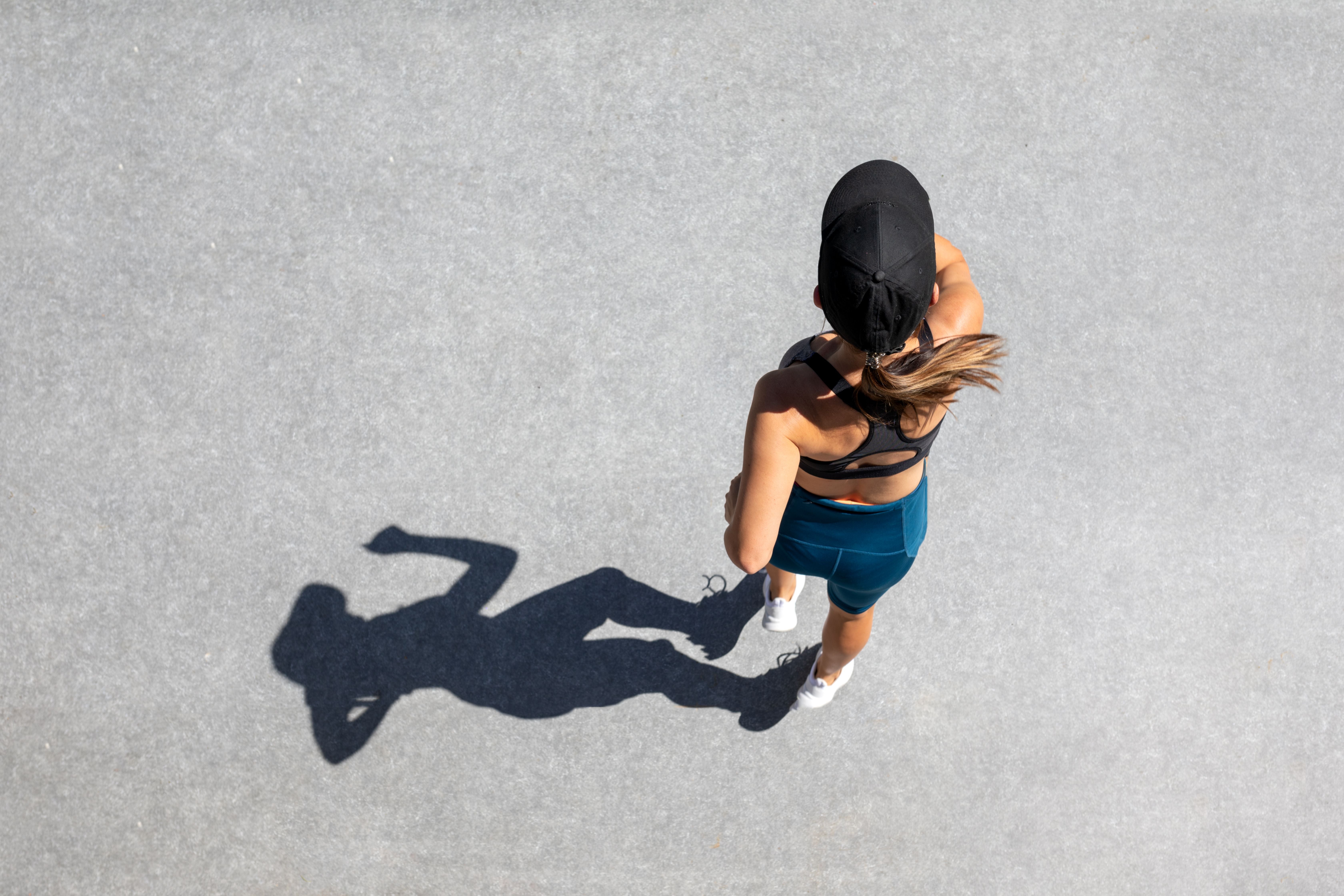 Frau joggt im Sommer auf hellem Boden, fotografiert von oben mit Schattenwurf.