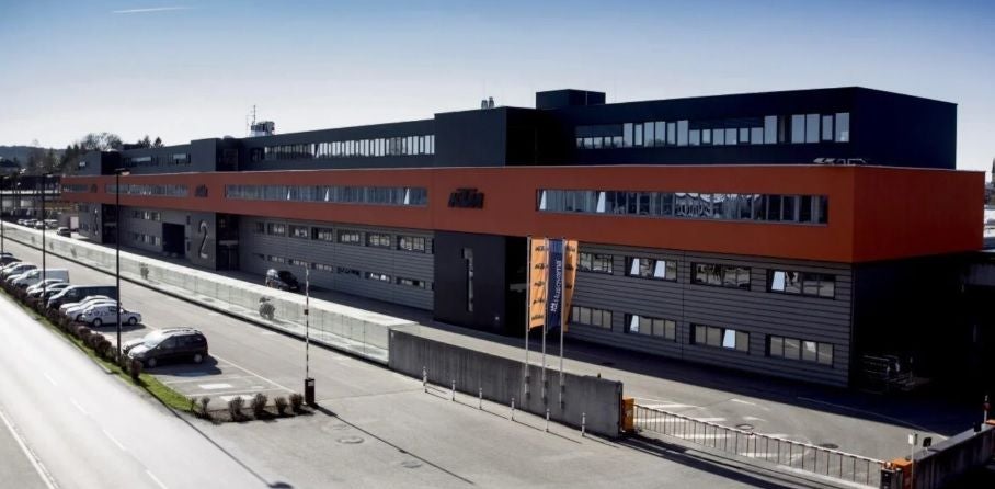 Modernes KTM-Firmengebäude in Mattighofen mit geparkten Autos und Fahnen davor.
