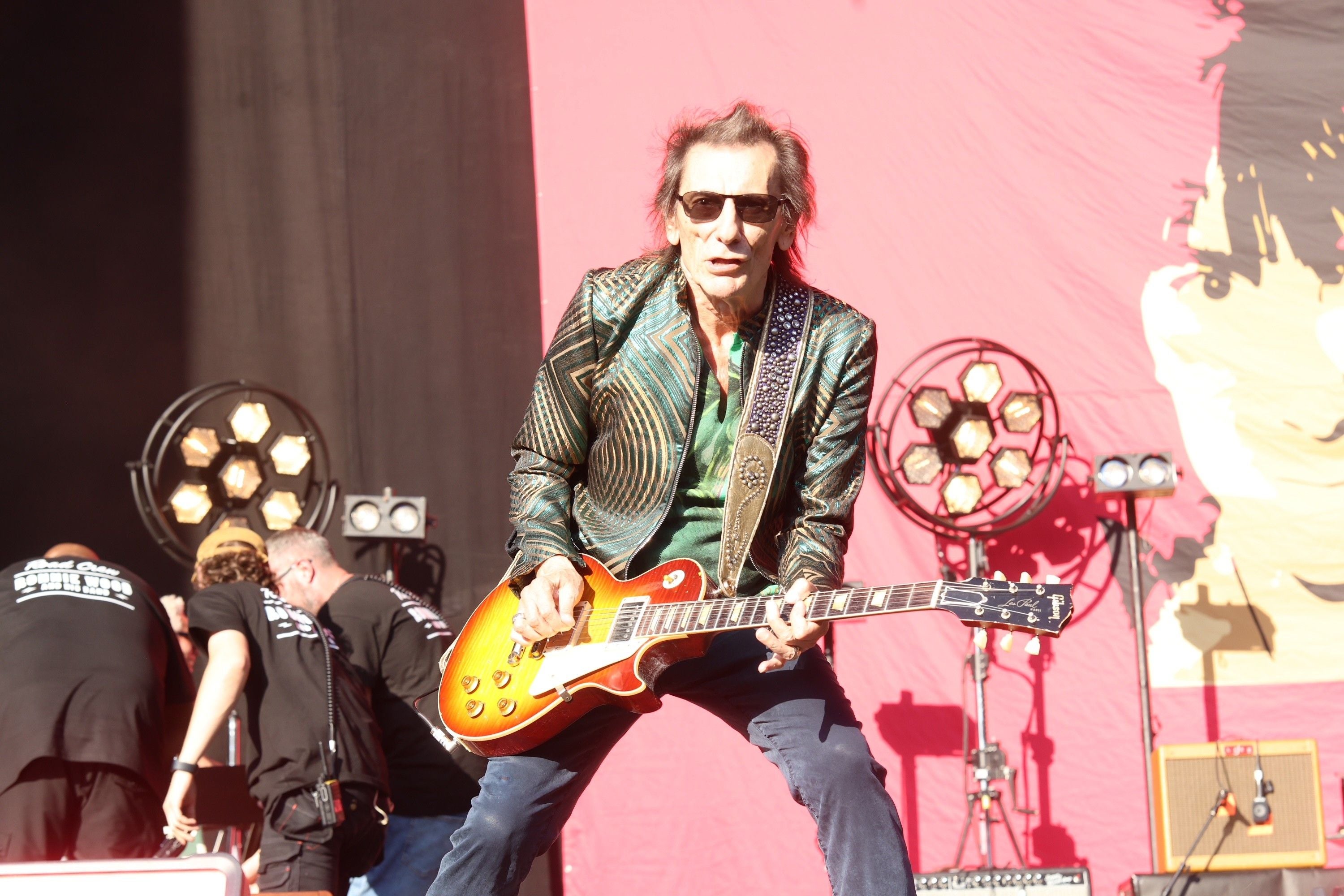 Ronnie Wood spielt E-Gitarre auf einer Bühne vor rotem Hintergrund.