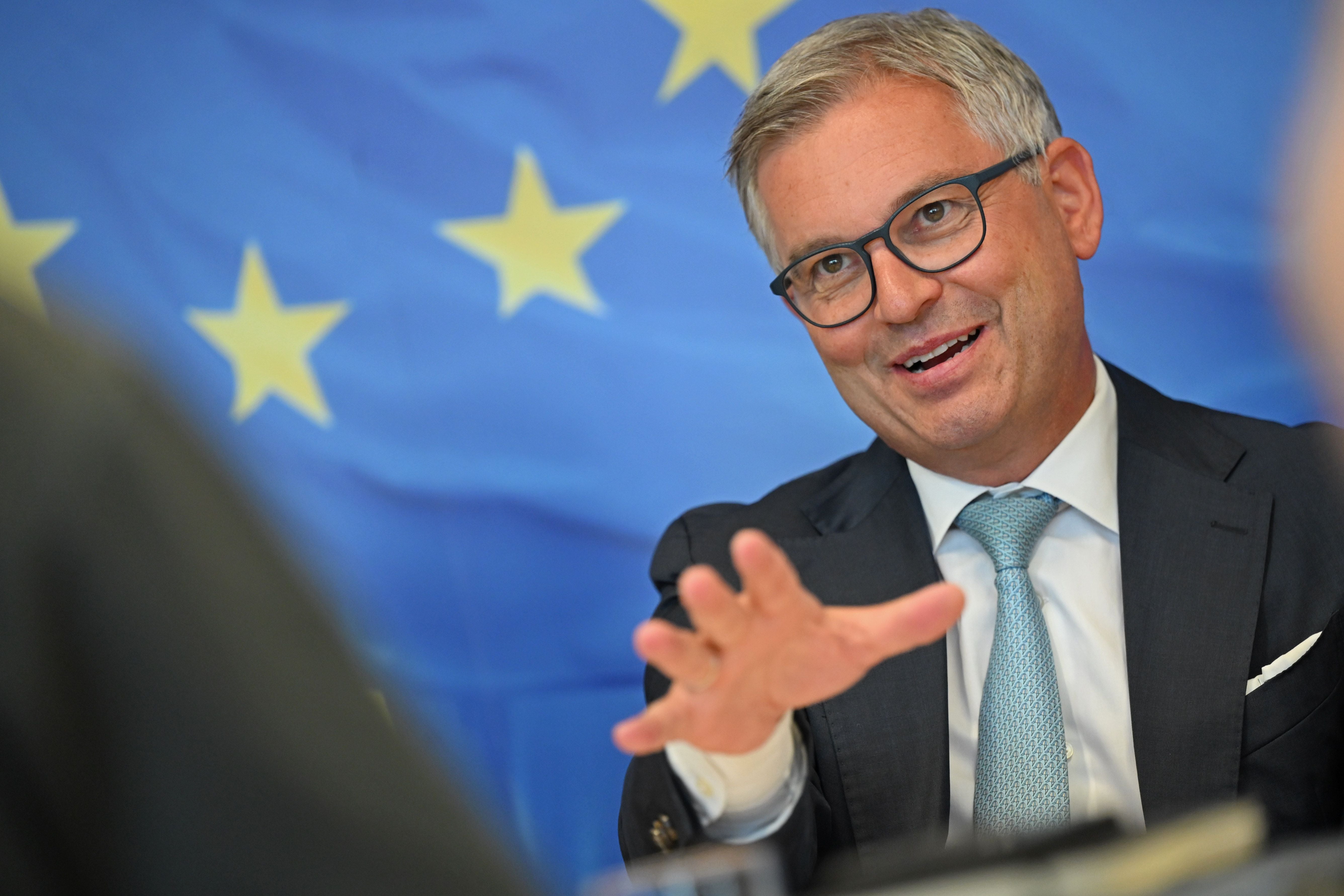 Ein Mann im Anzug spricht gestikulierend vor einer EU-Flagge im Hintergrund.