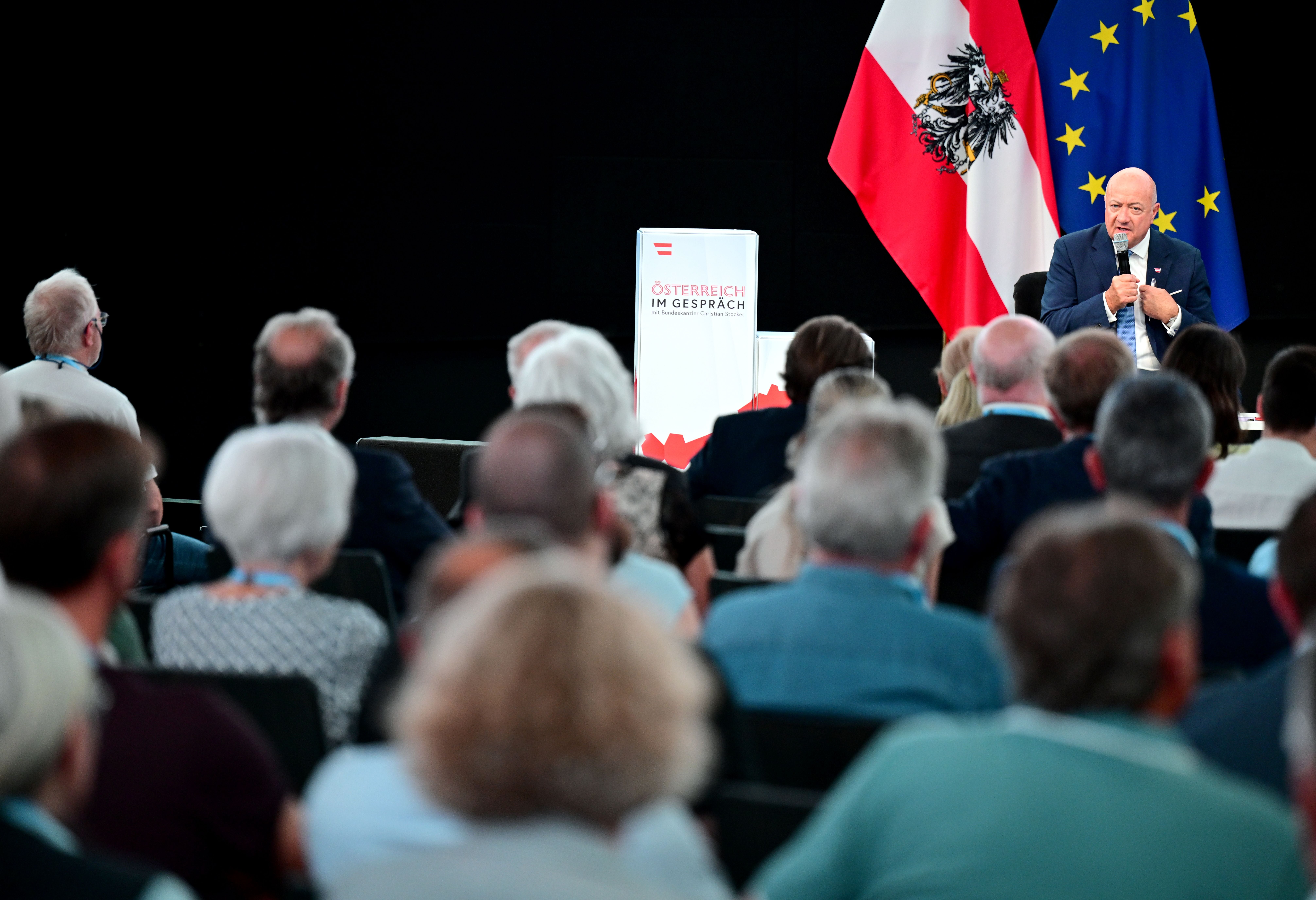 Bundeskanzler spricht vor Publikum, hinter ihm österreichische und EU-Flagge.