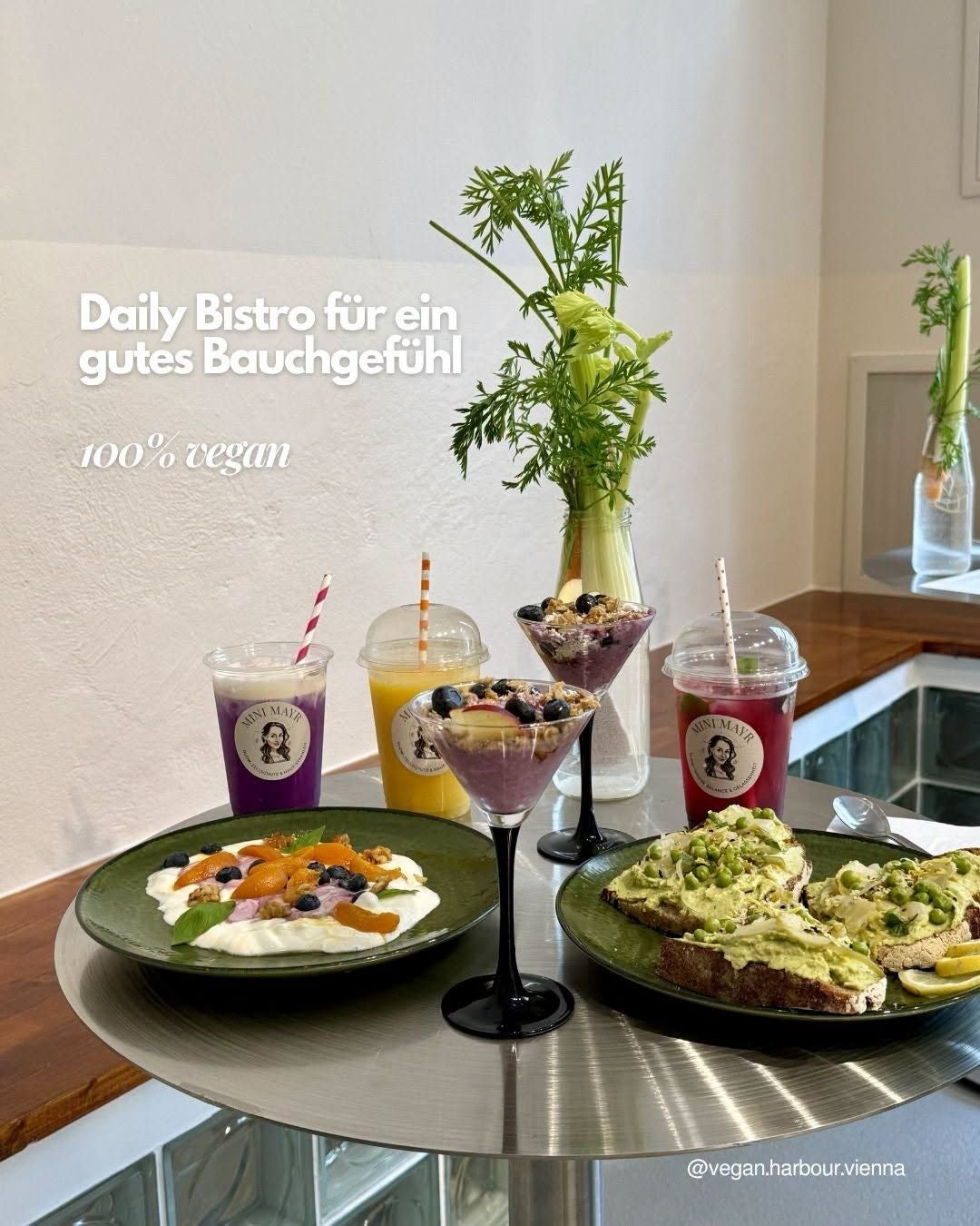 Veganes Frühstück mit Smoothies, Avocado-Toast, Joghurt und Obst auf einem Tisch im Bistro.