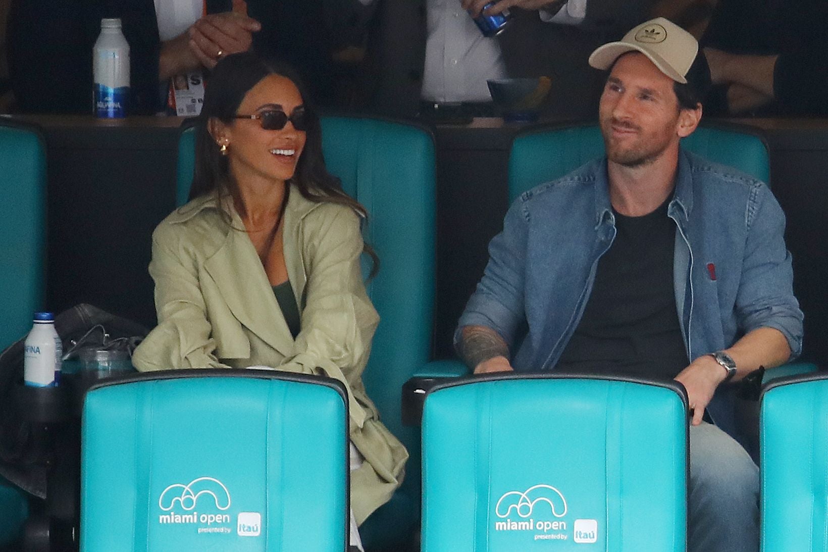 Ein Mann und eine Frau sitzen lächelnd auf türkisfarbenen Sitzen beim Miami Open Tennisturnier.