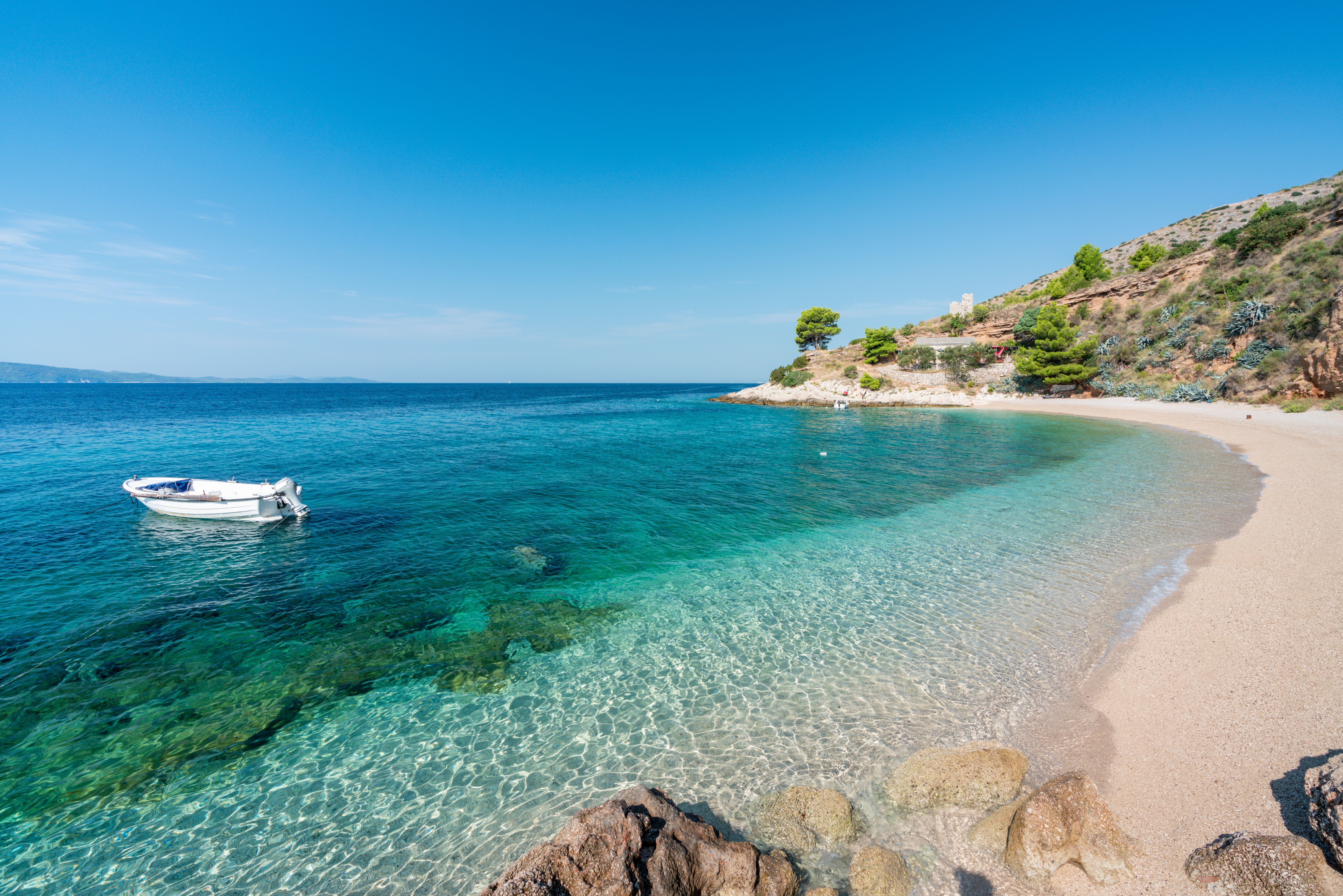 Klares türkisblaues Meer mit kleinem Boot und Sandstrand bei Murvica auf der Insel Brac.