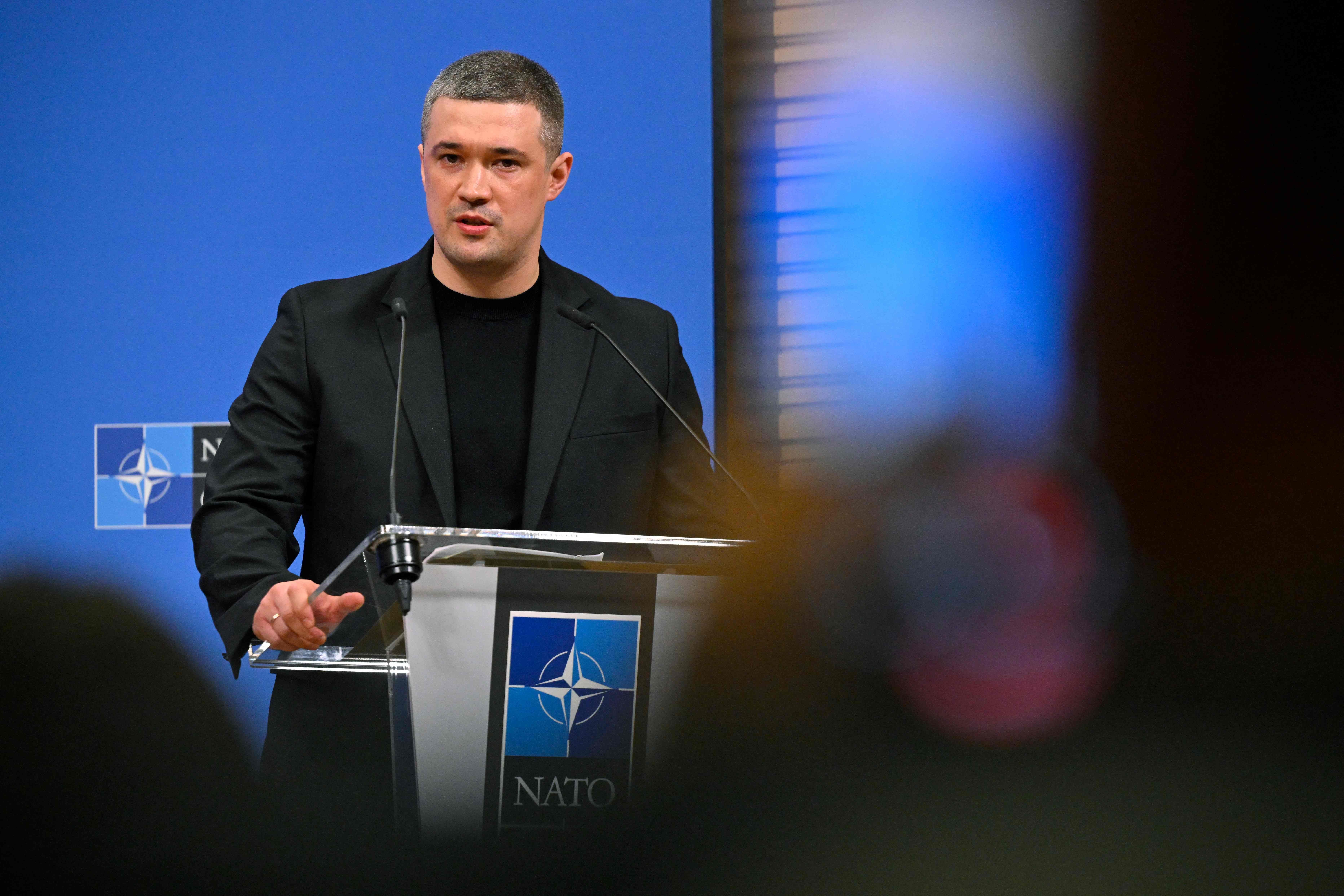 Ein Mann spricht am NATO-Pult bei einer Pressekonferenz vor blauem Hintergrund.