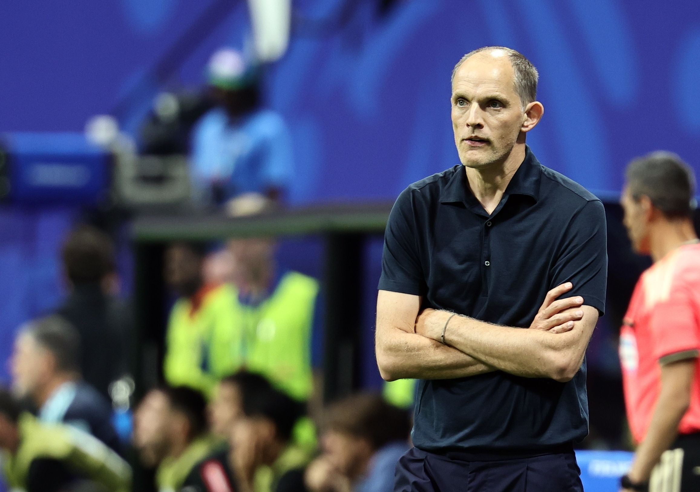 Ein Fußballtrainer steht mit verschränkten Armen am Spielfeldrand während eines Spiels.