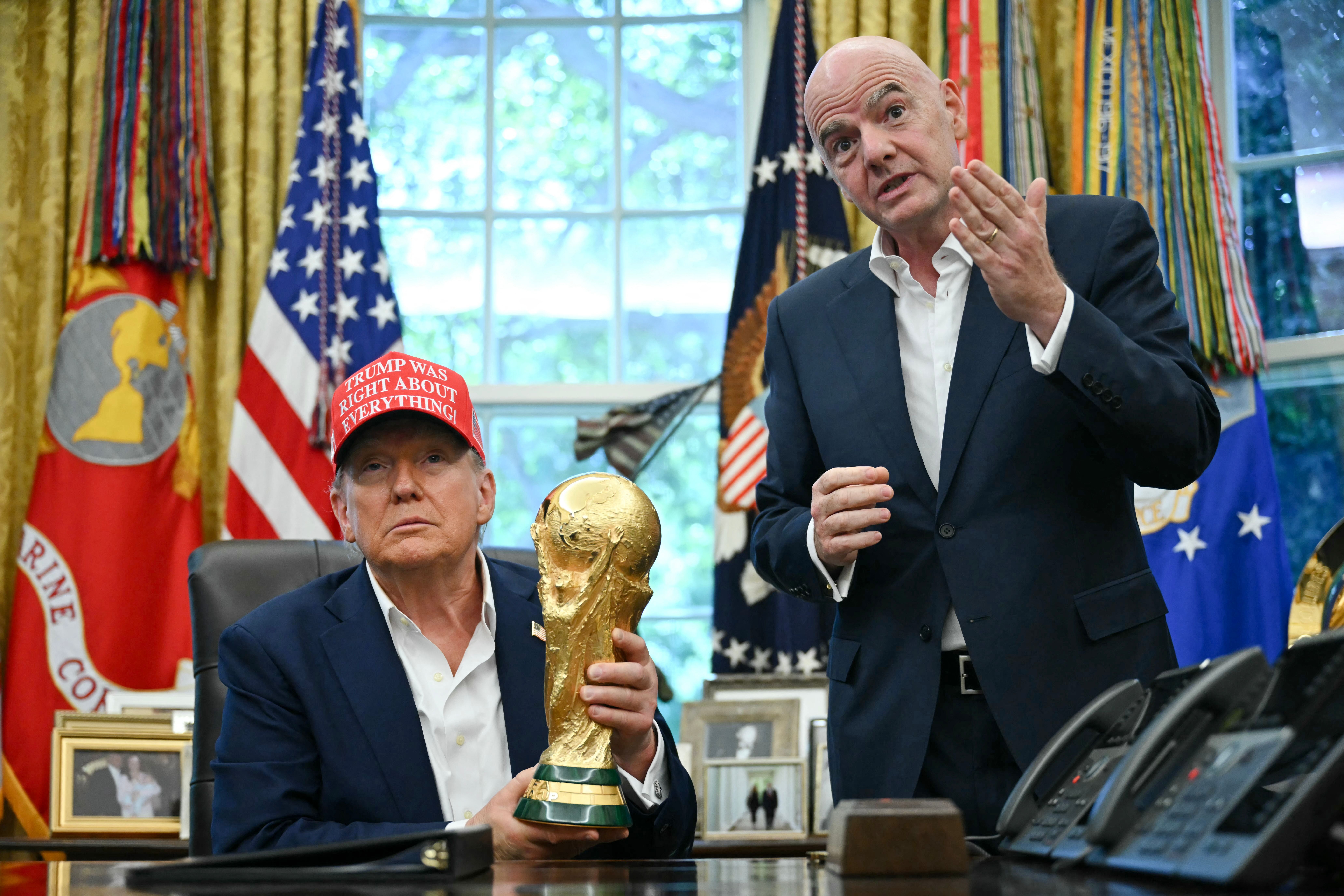 Donald Trump hält im Oval Office den WM-Pokal, daneben steht Gianni Infantino und gestikuliert.