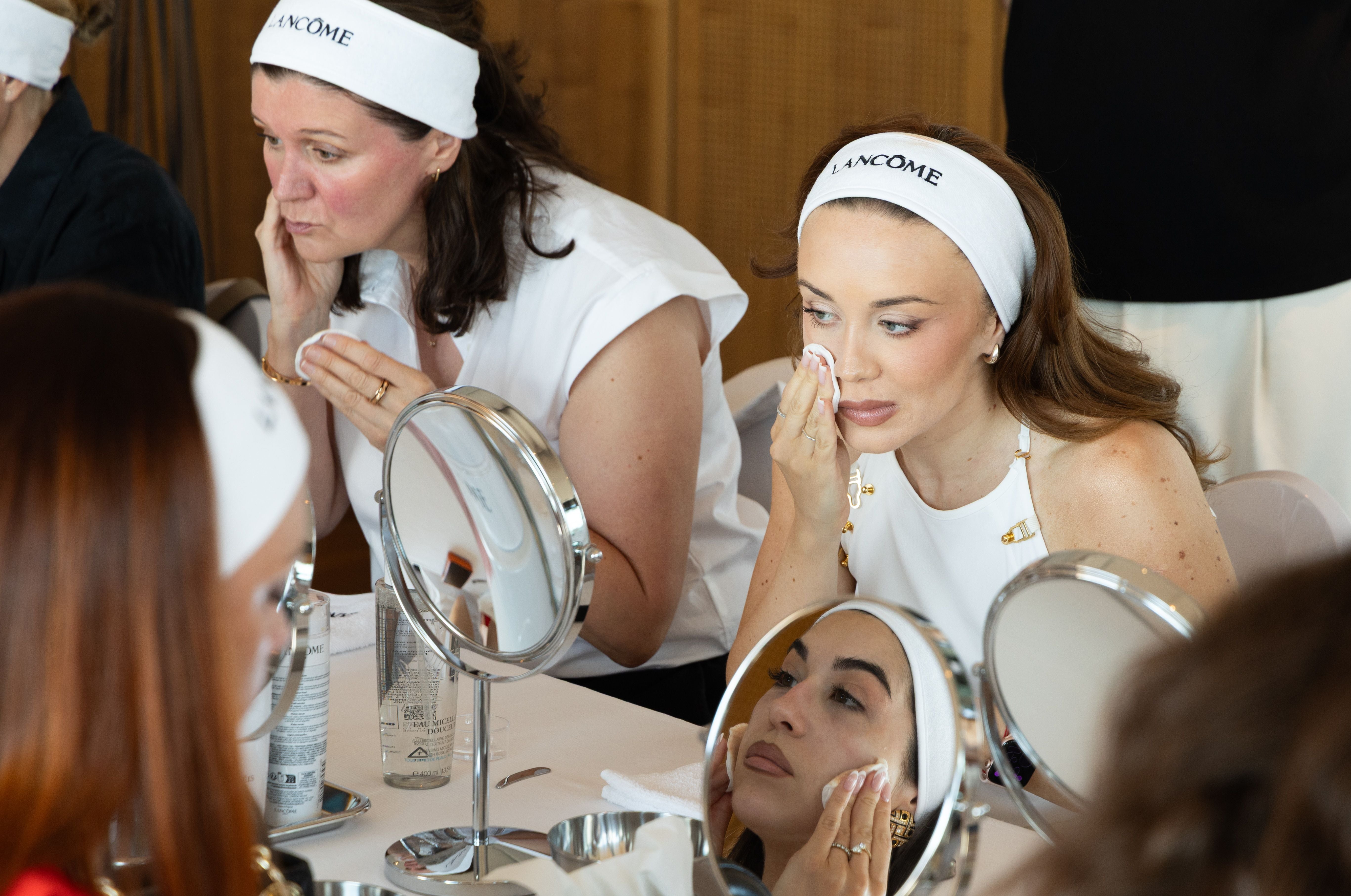 Frauen tragen Stirnbänder und reinigen ihr Gesicht bei einer Beauty-Masterclass vor Spiegeln.