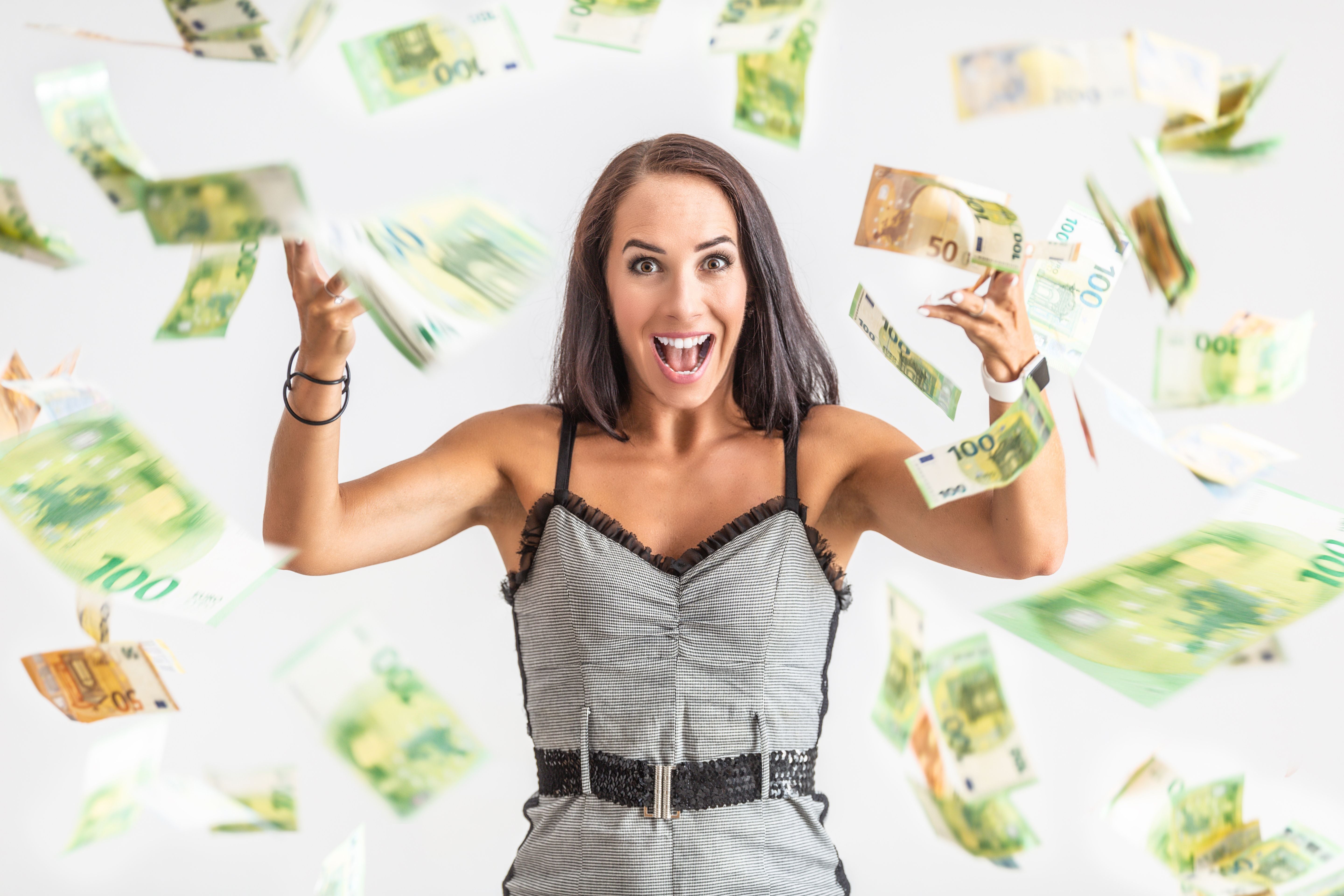 Junge Frau wirft viele Euro-Banknoten begeistert in die Luft.