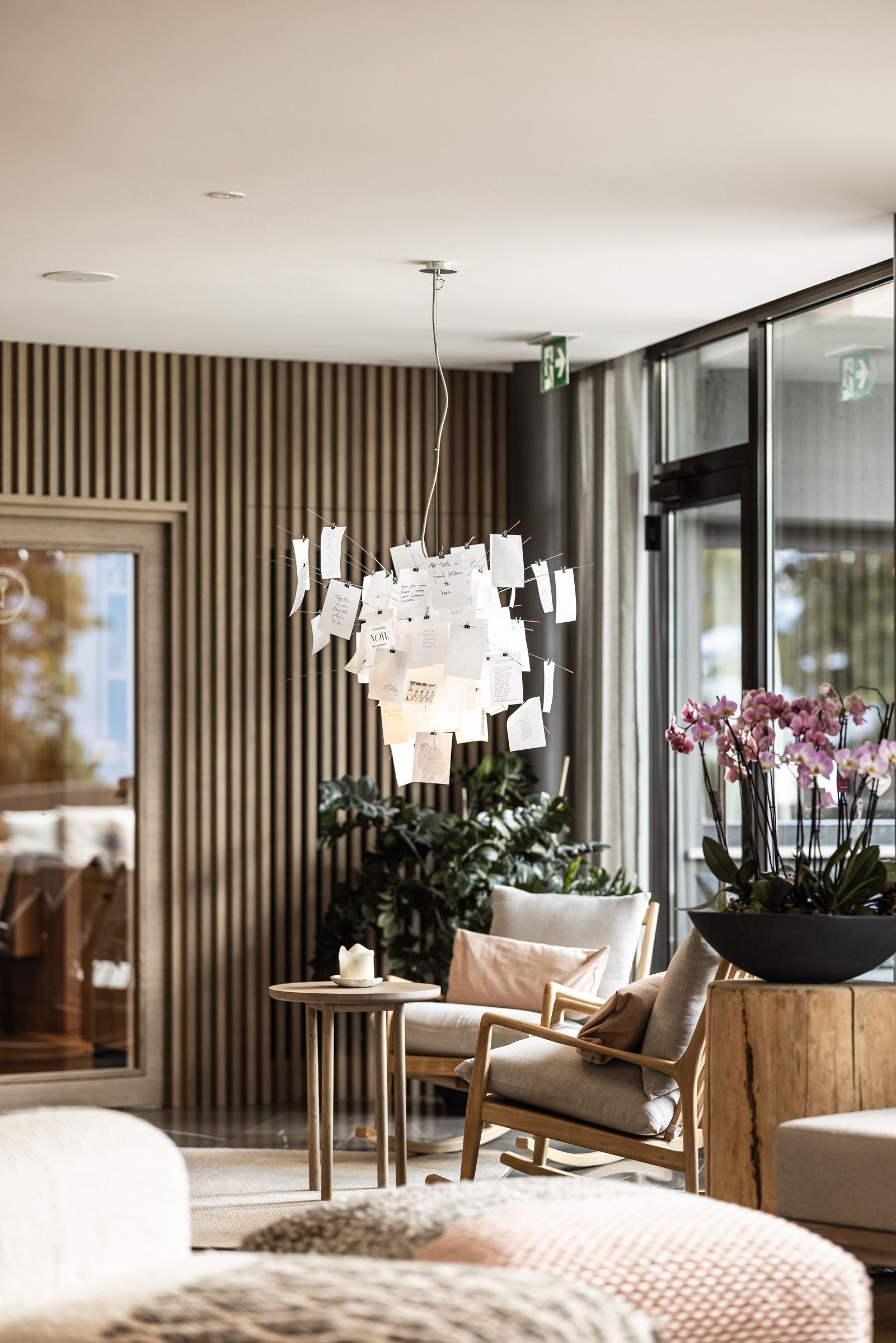 Gemütliche Hotellounge mit Sesseln, Tisch, Pflanzen, Orchideen und einer Lampe mit Zetteln.