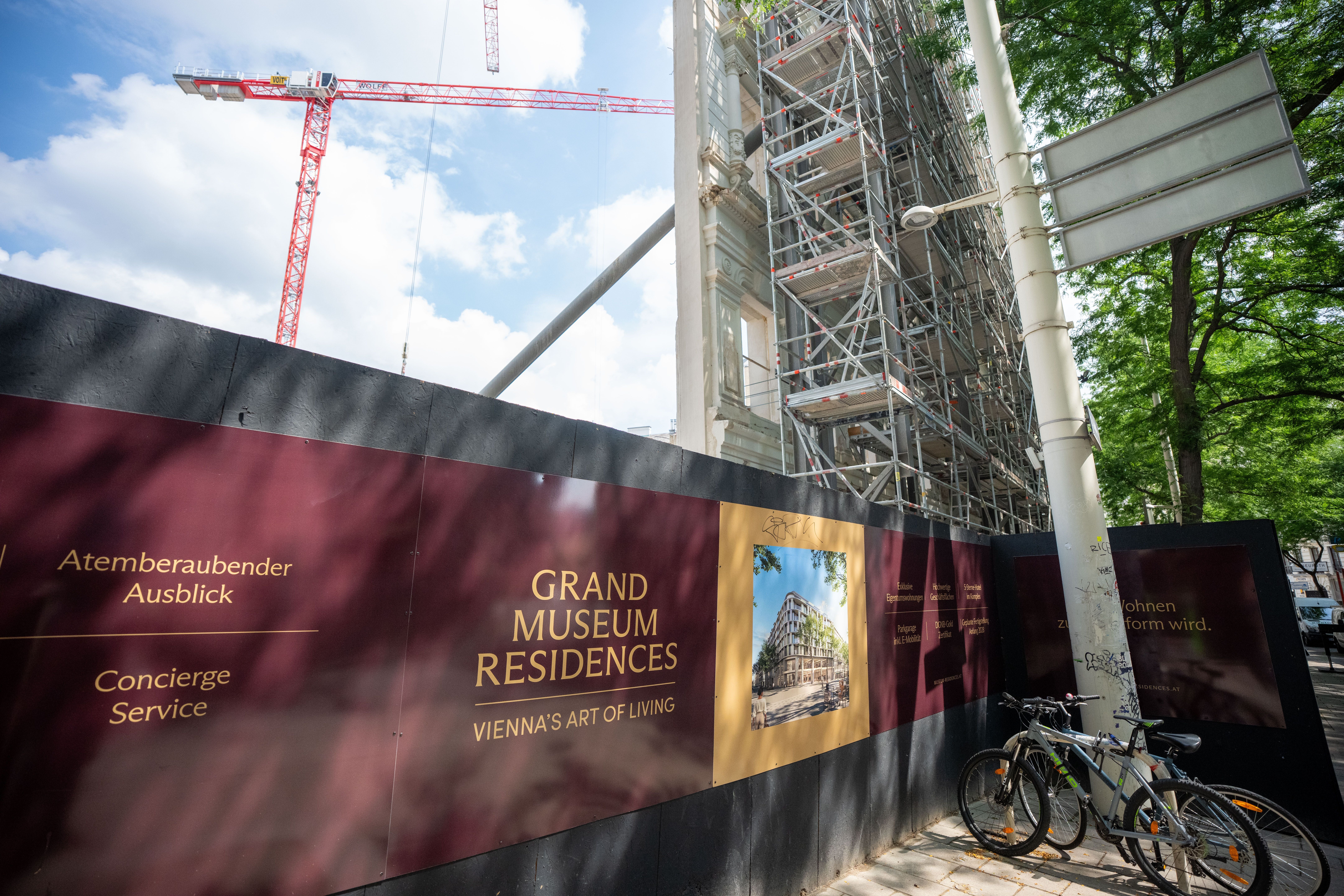 Absperrzaun mit Werbung für "Grand Museum Residences" vor Baustelle mit Gerüst und Kran in Wien.