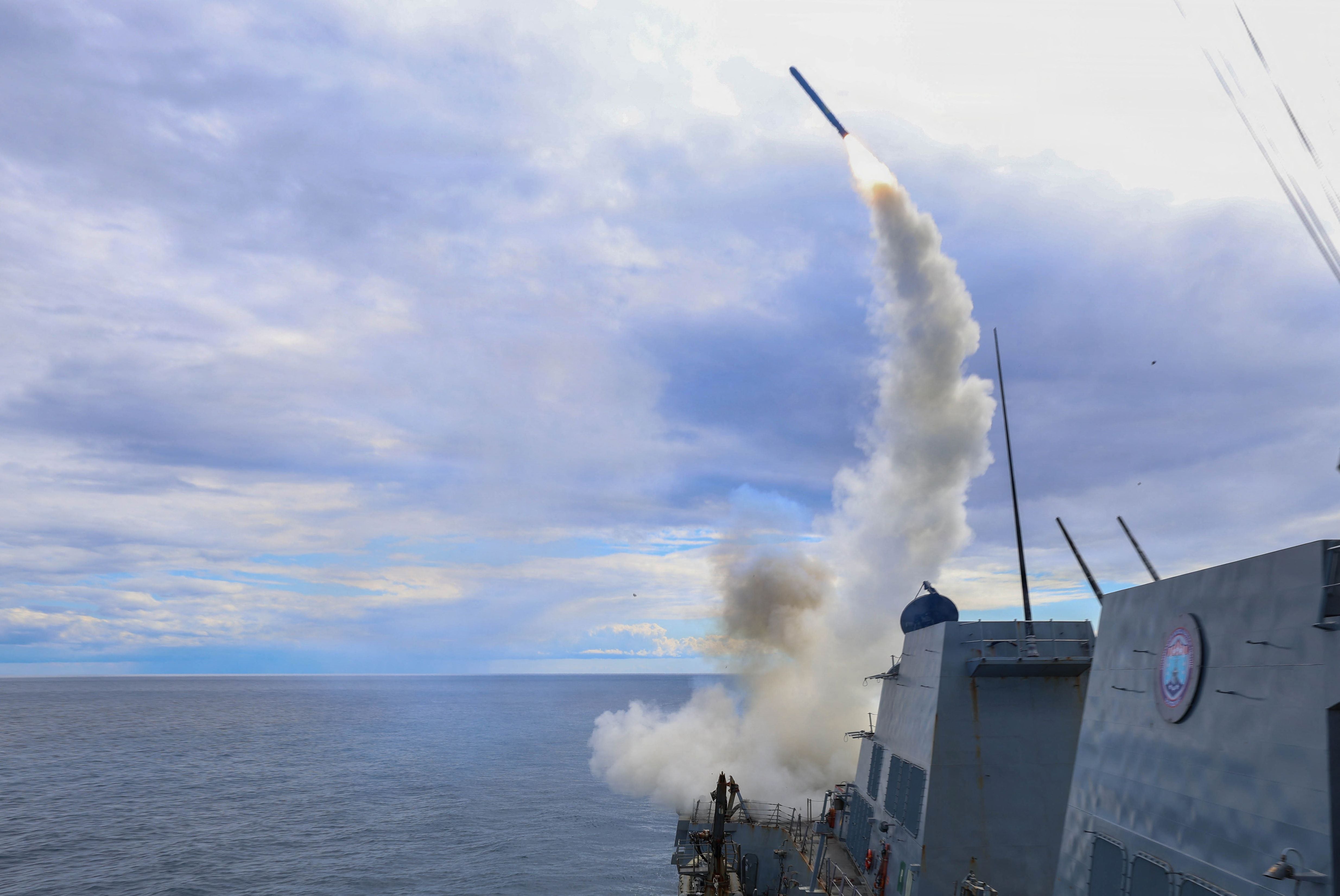 Ein Kriegsschiff feuert eine Rakete über das Meer, Rauch steigt hinter dem Schiff auf.