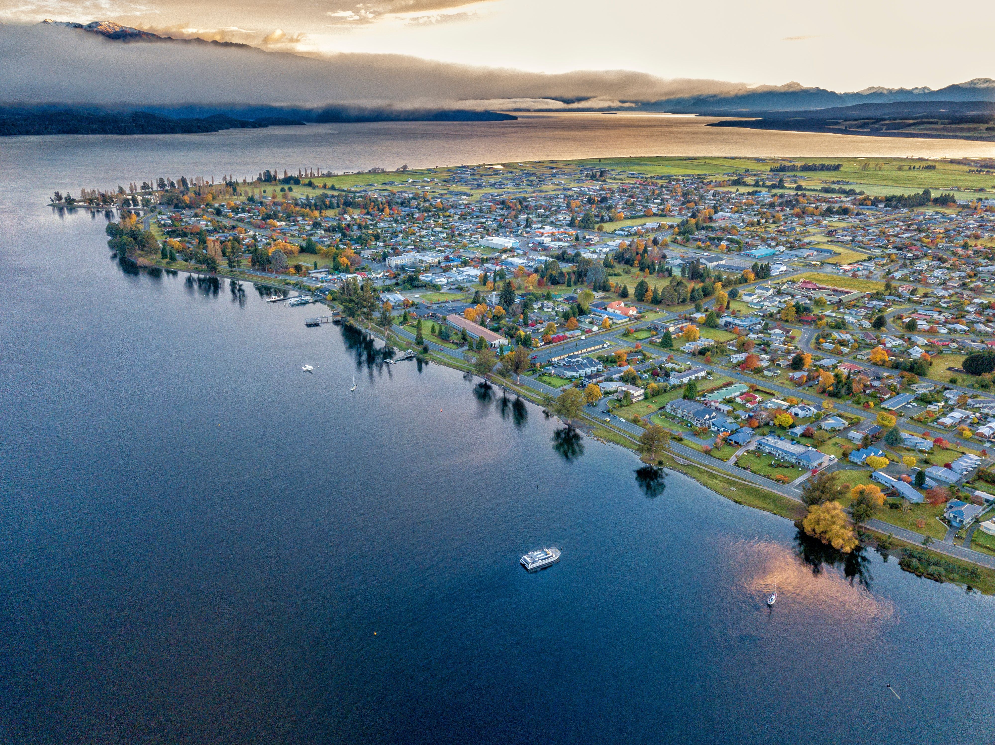 Luftaufnahme von Te Anau am See in Neuseeland im Herbst, mit Booten auf dem Wasser.