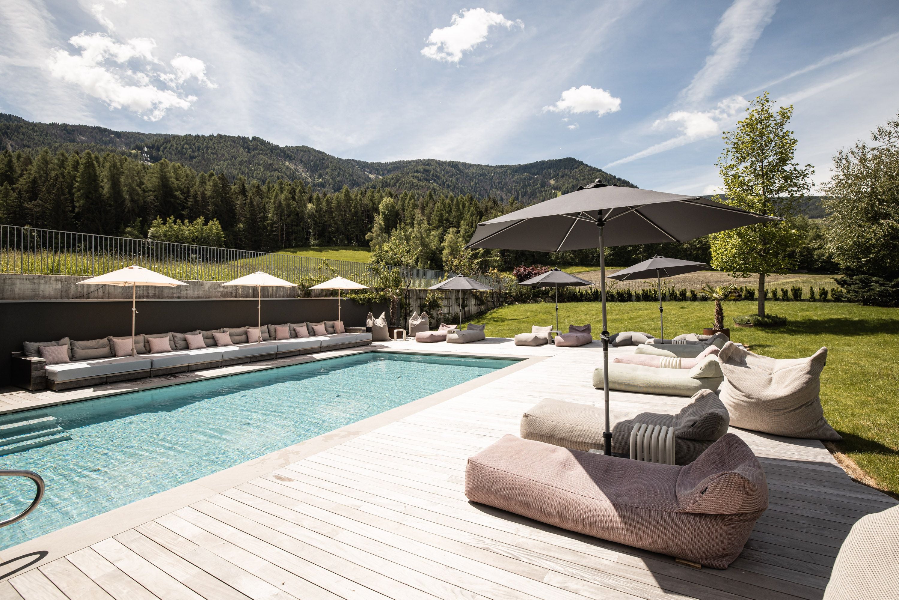 Moderner Außenpool mit Sonnenliegen, Sonnenschirmen und Blick auf grüne Berge im Hotel Petrus.