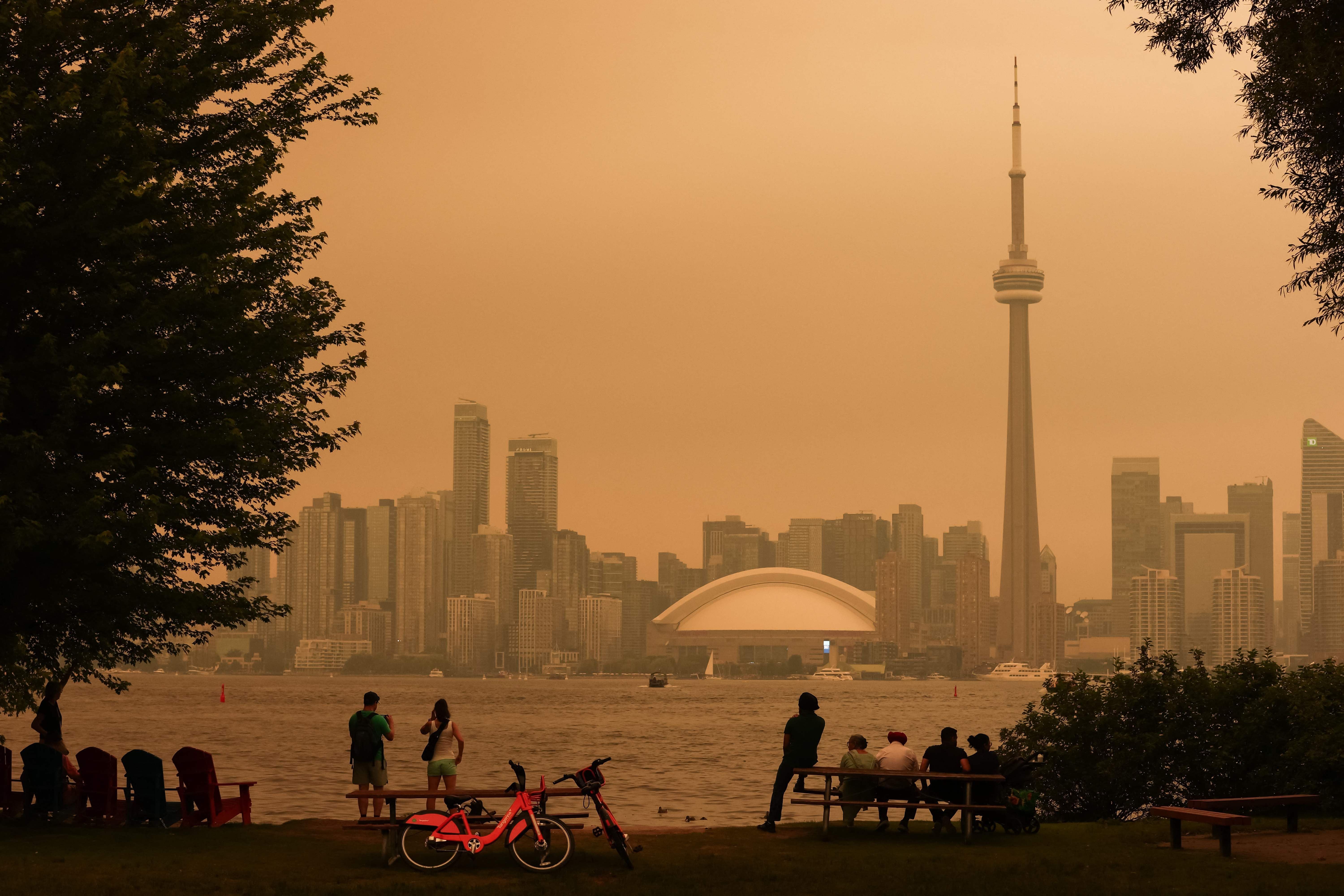 Menschen betrachten Torontos Skyline unter gelbem Rauch durch Waldbrände, Luft ist dunstig und trüb.
