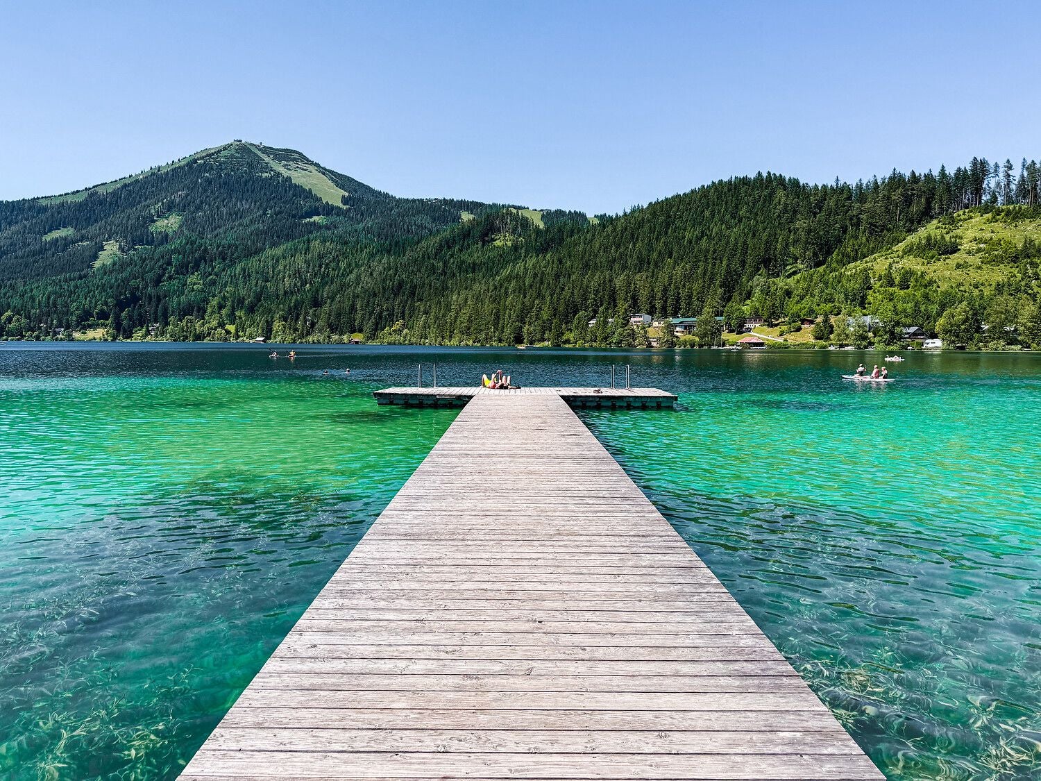 Steg führt über türkisgrünen Erlaufsee, umgeben von bewaldeten Bergen und klarem Himmel.