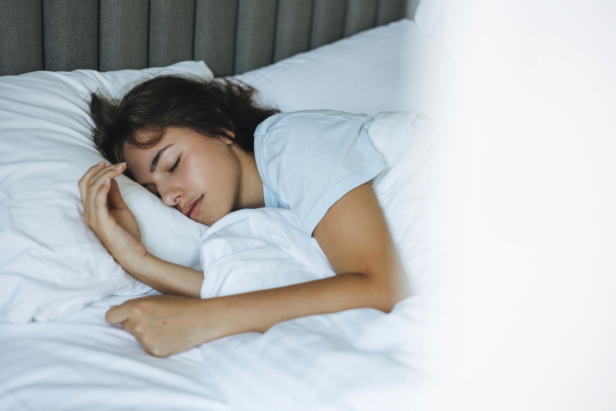 Junge Frau schläft friedlich in einem Bett mit weißen Decken und sieht entspannt aus.