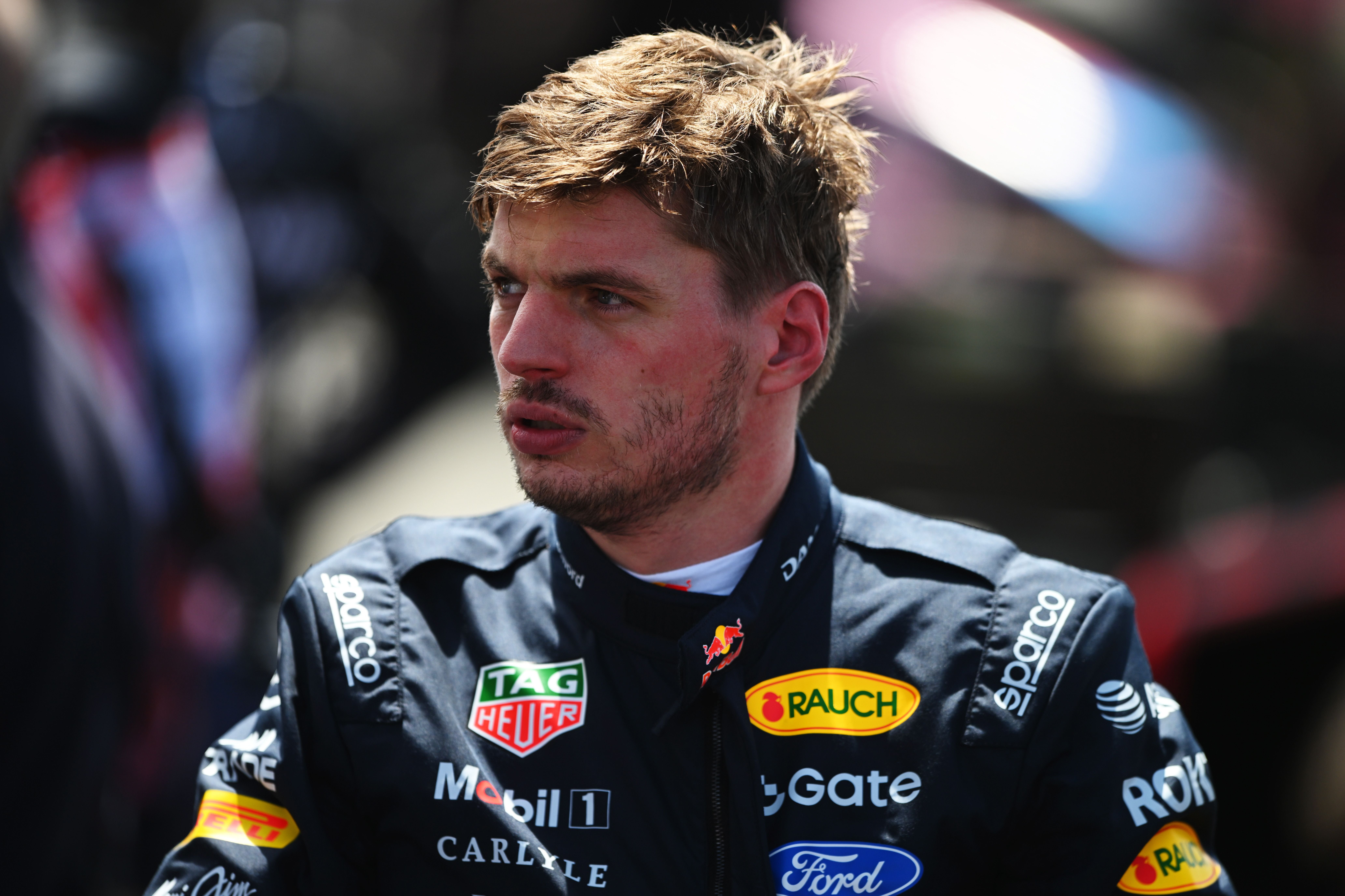 Ein Rennfahrer im Red Bull Racing Anzug steht nachdenklich im Parc Fermé bei Tageslicht.