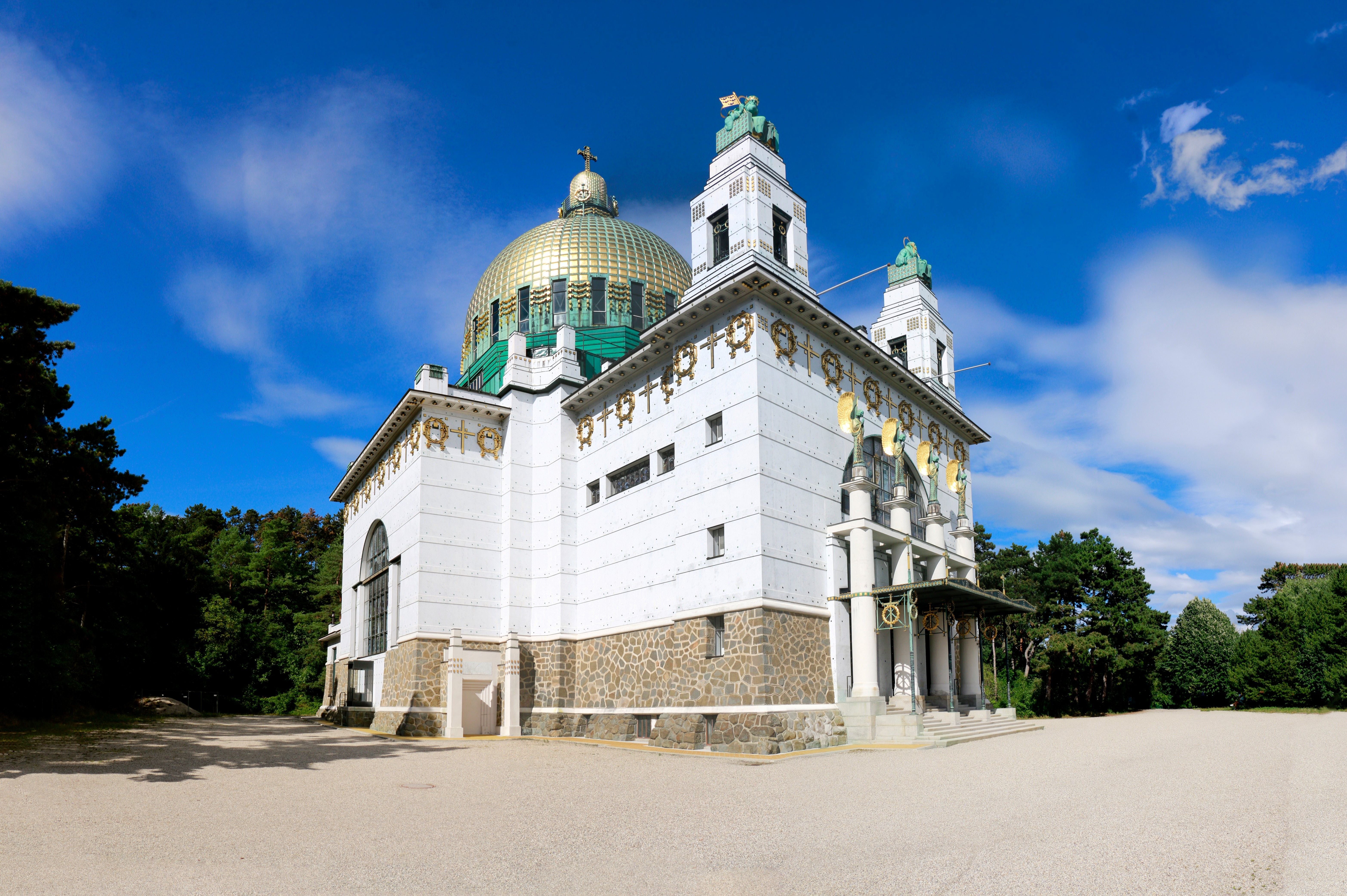 Weiße Kirche im Art-Deco-Stil mit goldener Kuppel vor blauem Himmel in Wien, Österreich.