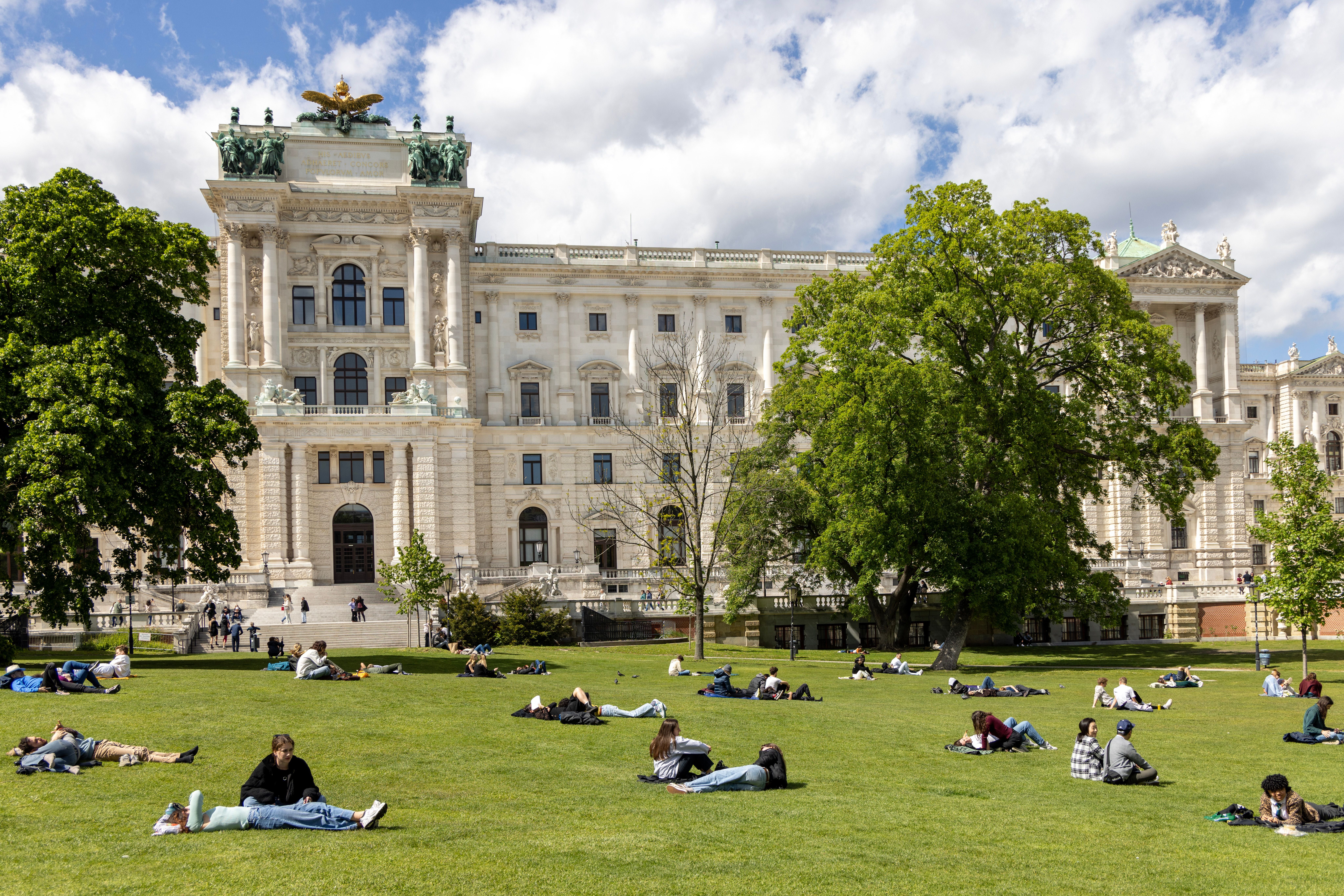 Menschen liegen auf der Wiese im Burggarten vor der Hofburg in Wien an einem sonnigen Tag.