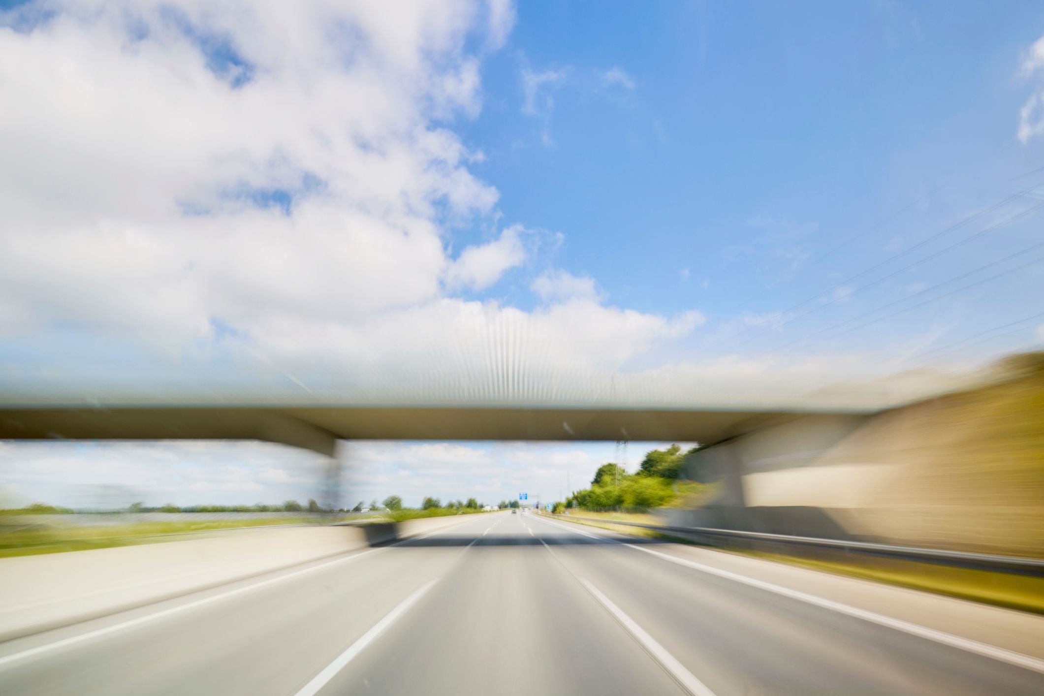 Verschwommene Aufnahme einer Autobahn mit Brücke unter blauem Himmel und einigen Wolken.