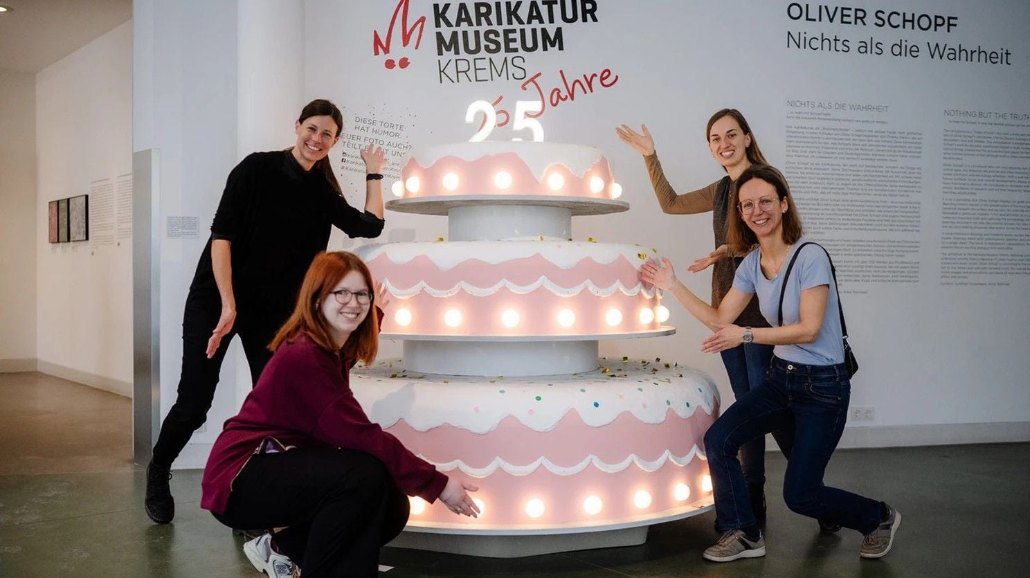 Vier Frauen posieren an einer großen, dekorativen Geburtstagstorte im Karikaturmuseum Krems.