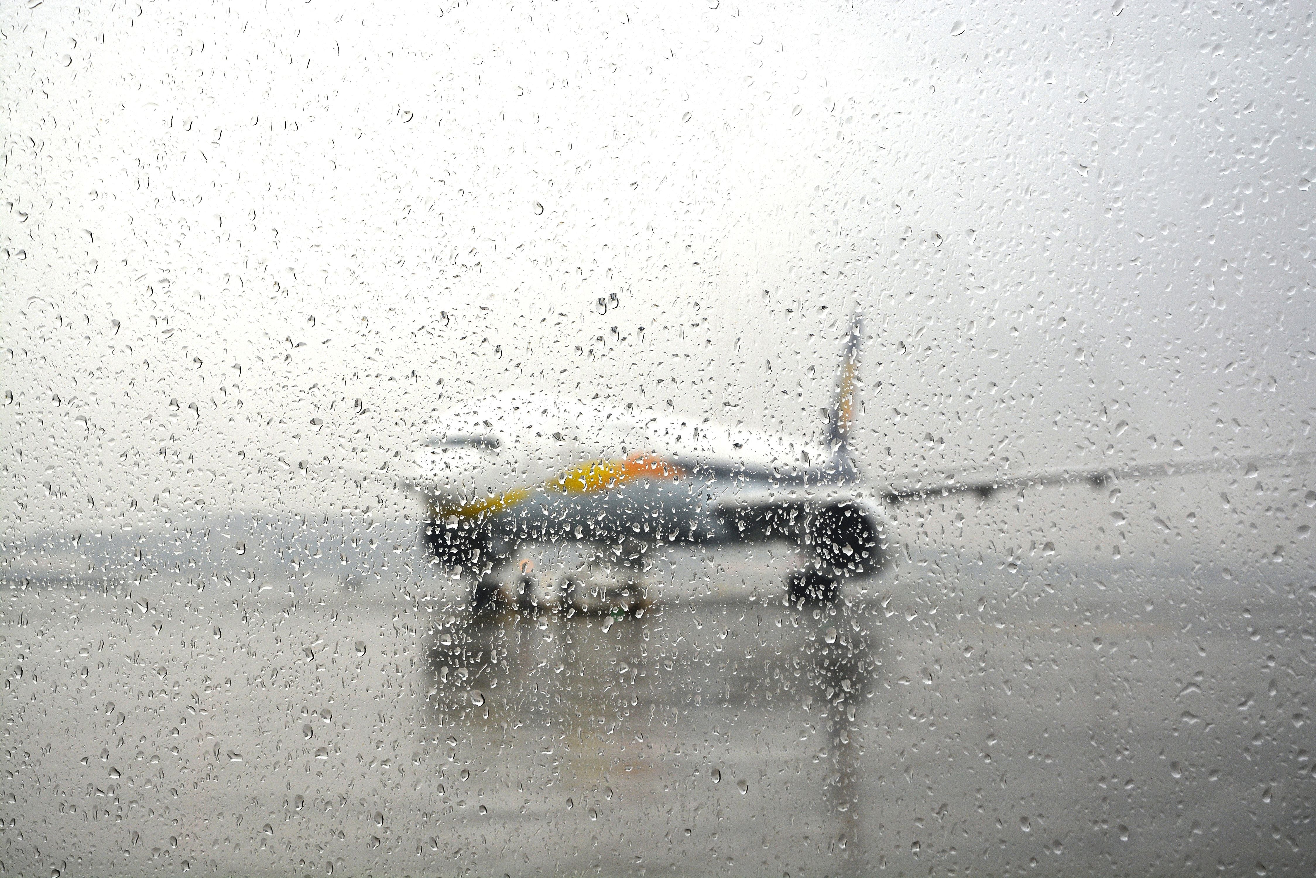 Regentropfen auf Fensterscheibe, im Hintergrund ein Flugzeug bei Regen am Flughafen.