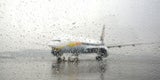 Regentropfen auf Fensterscheibe, im Hintergrund ein Flugzeug bei Regen am Flughafen.