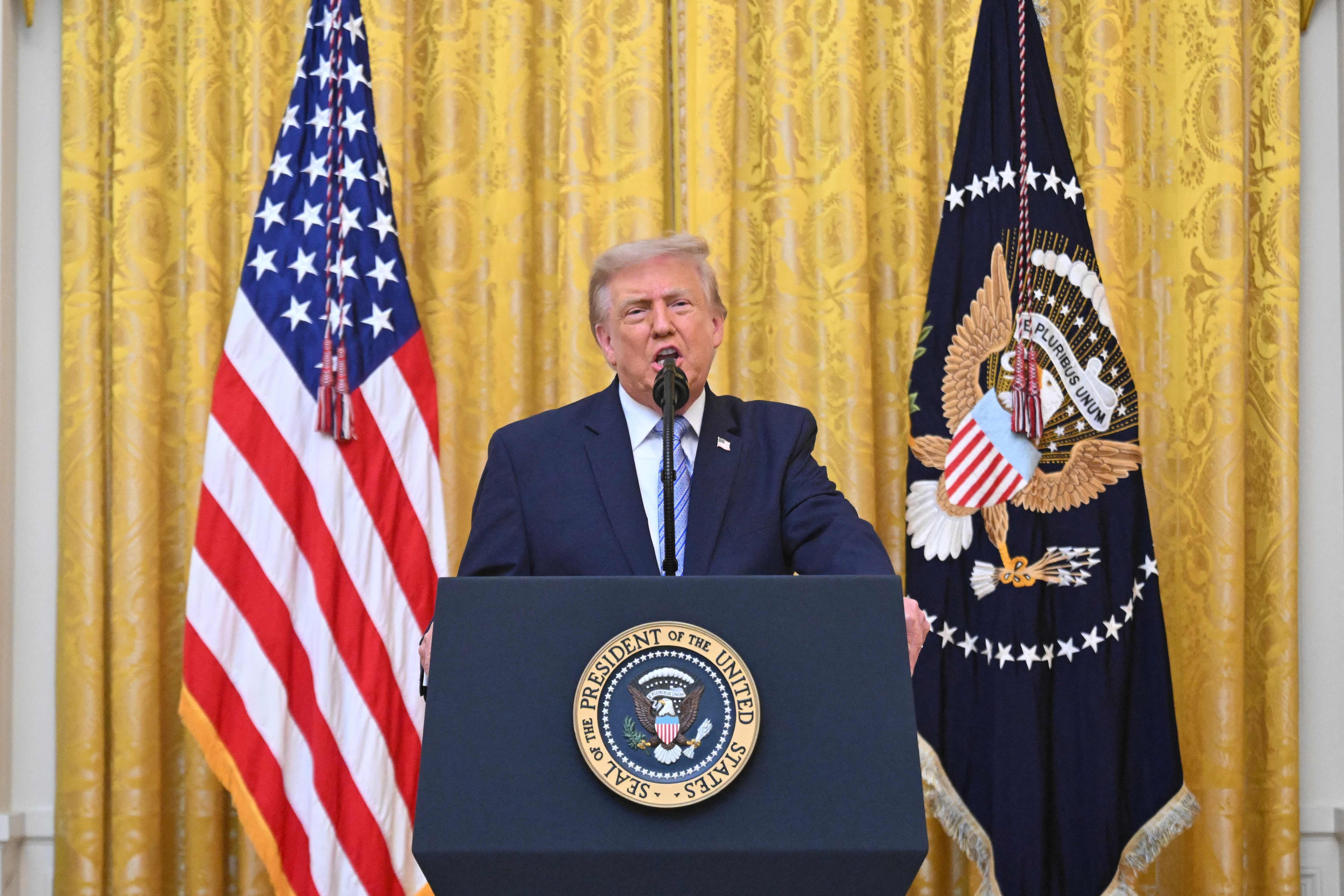 Ein Mann hält eine Rede am Rednerpult des US-Präsidenten vor US-Flaggen und goldenem Vorhang.