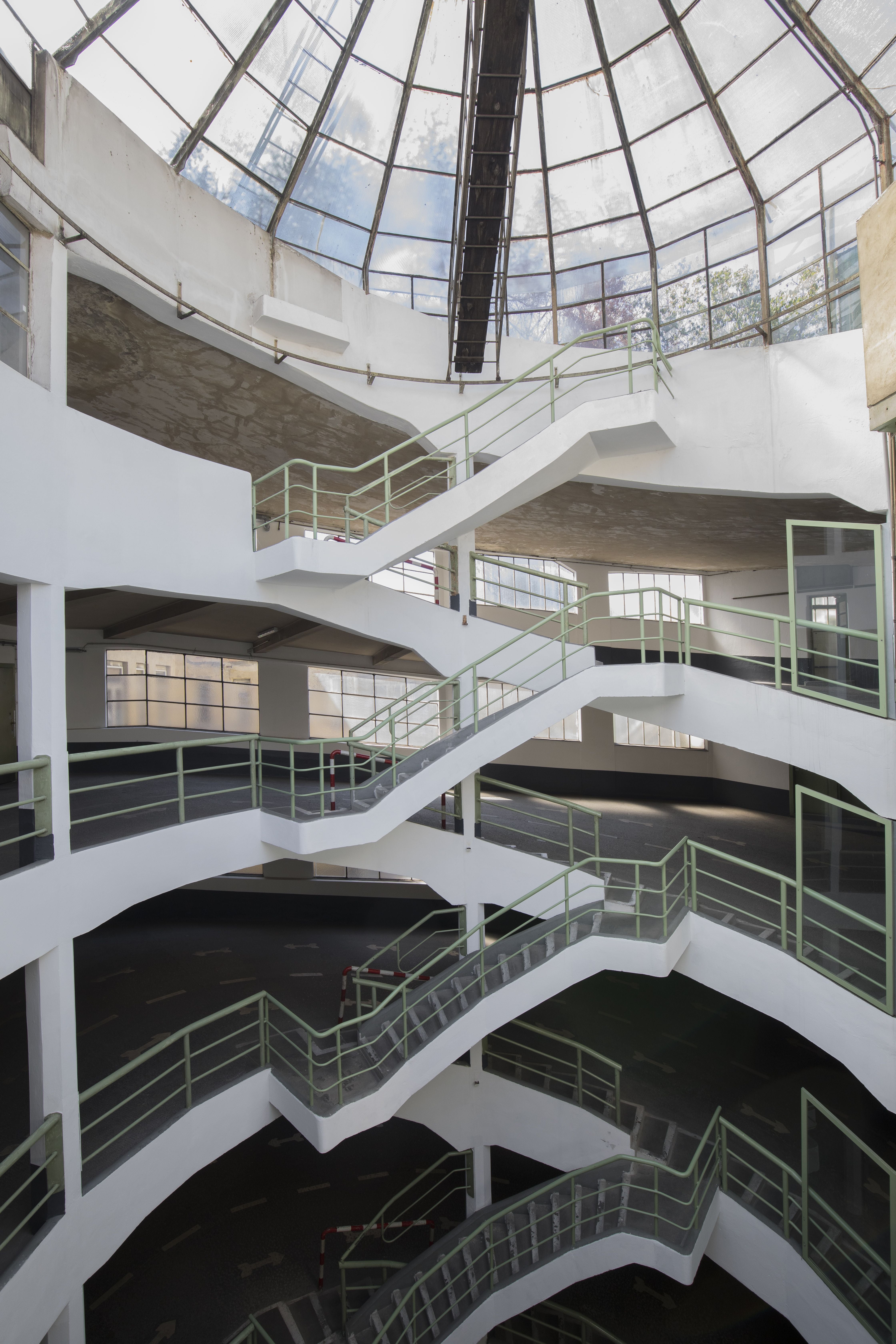 Mehrstöckiges Parkhaus mit weißen Wänden und grünem Geländer unter Glaskuppel.