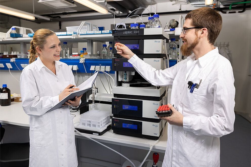 Zwei Wissenschaftler im Labor besprechen Daten vor Analysegeräten und Laborausrüstung.