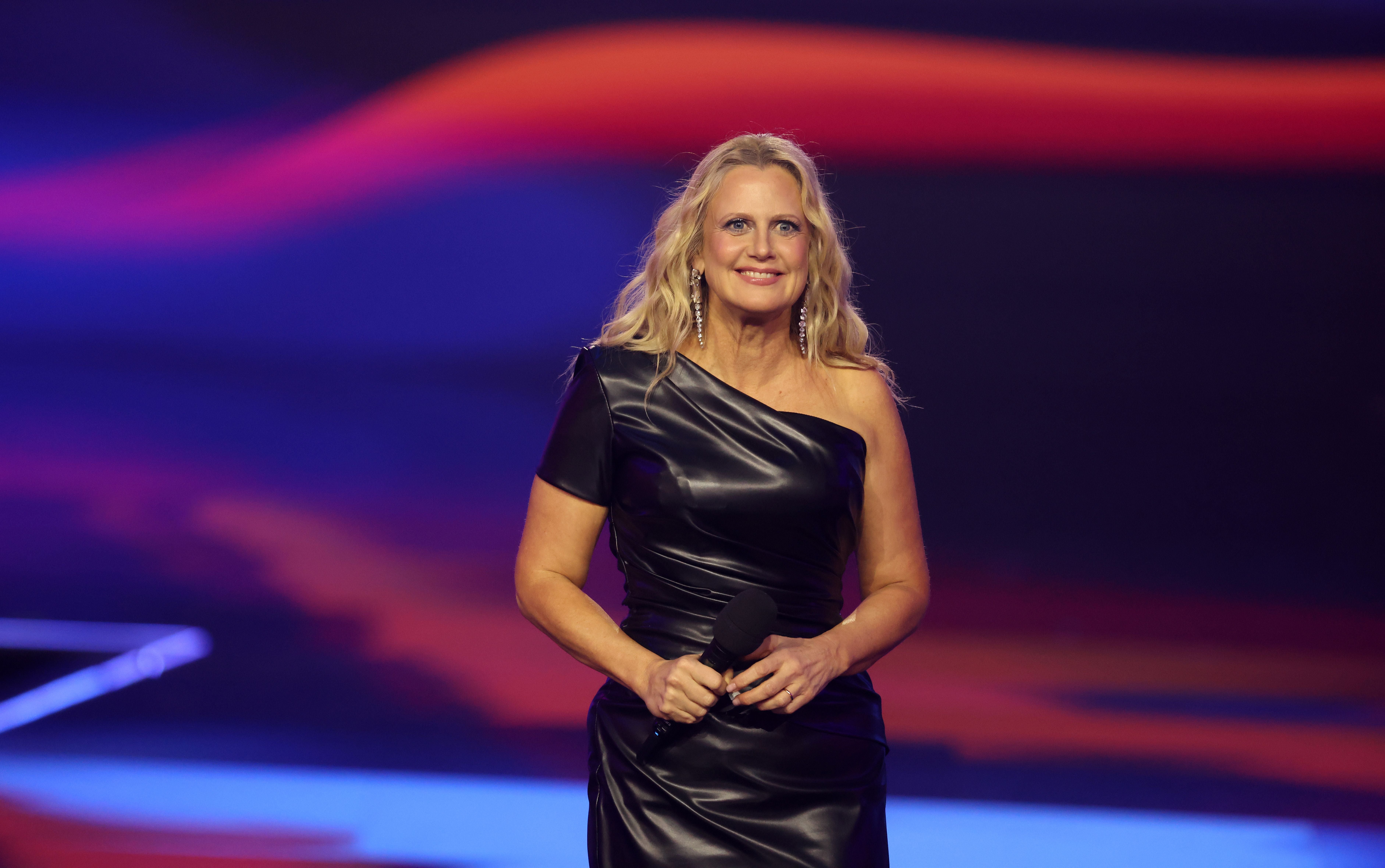 Eine Frau im schwarzen, schulterfreien Kleid hält ein Mikrofon auf einer Bühne.